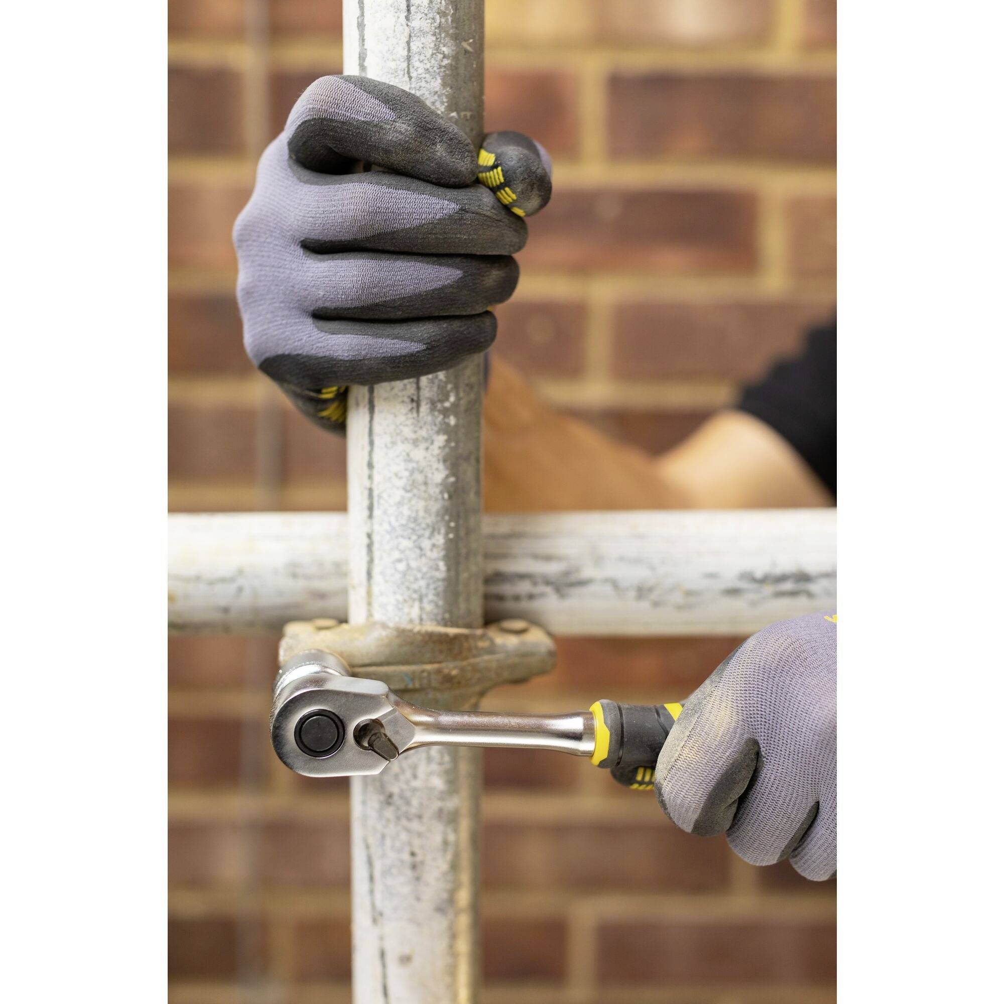Ruce v pracovních rukavicích používají klíč k utažení lešení před cihlovou zdí.