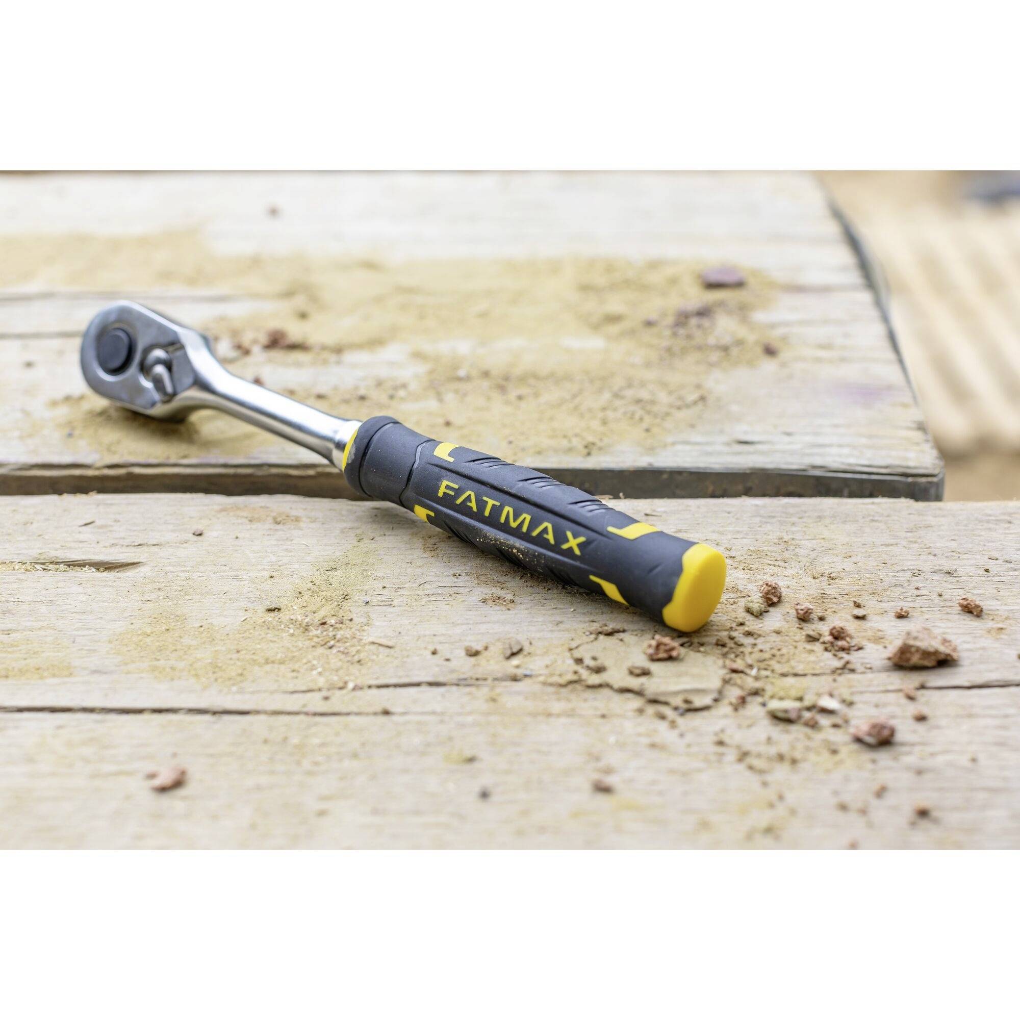 Žlutý a černý klíč leží na dřevěném pracovním stole s trochou písku a malými kamínky.