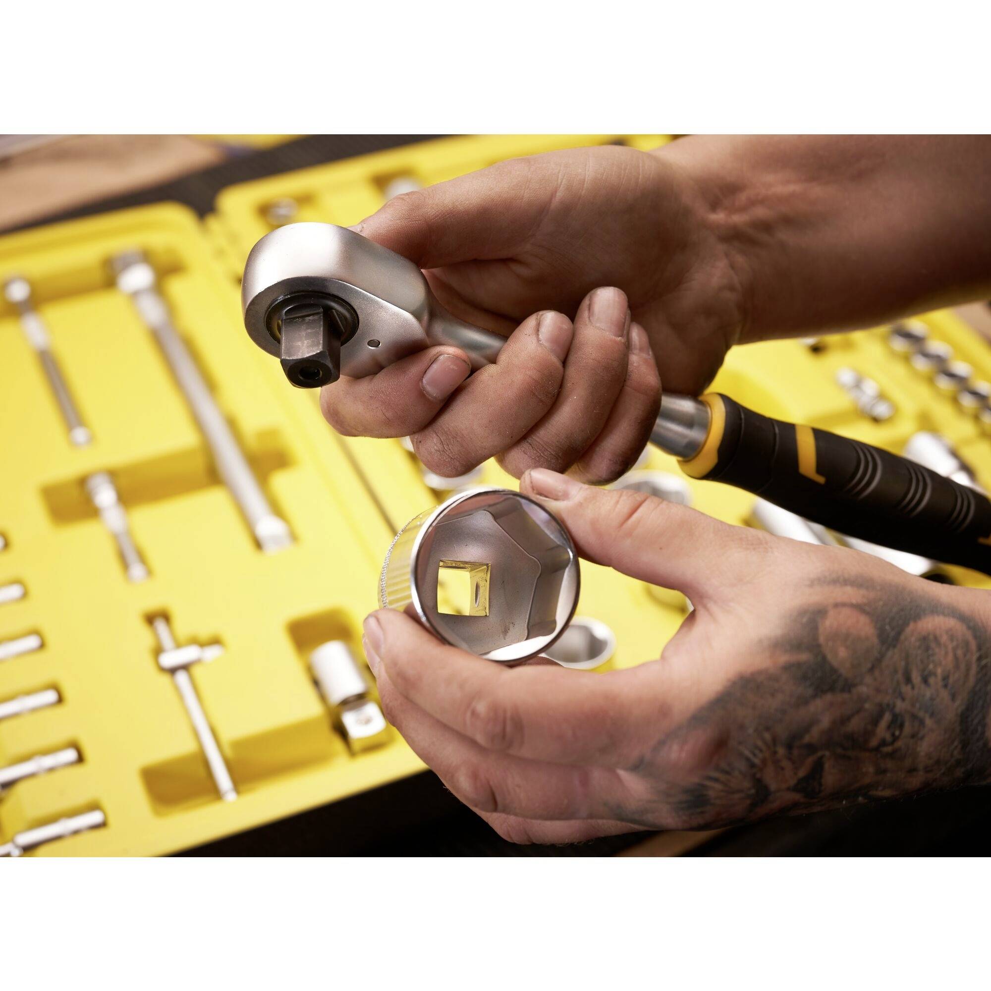 Jedna osoba drží ráčnu a příslušnou nástrčnou hlavici z otevřeného žlutého montážního kufříku.
