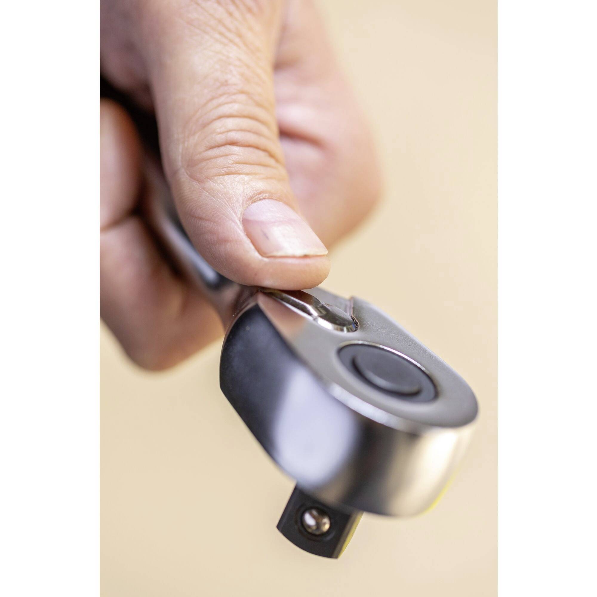 Jedna ruka drží stříbrný stavitelný klíč s černým tlačítkem. Zaostření je na rukojeti a kulatém kloubu.