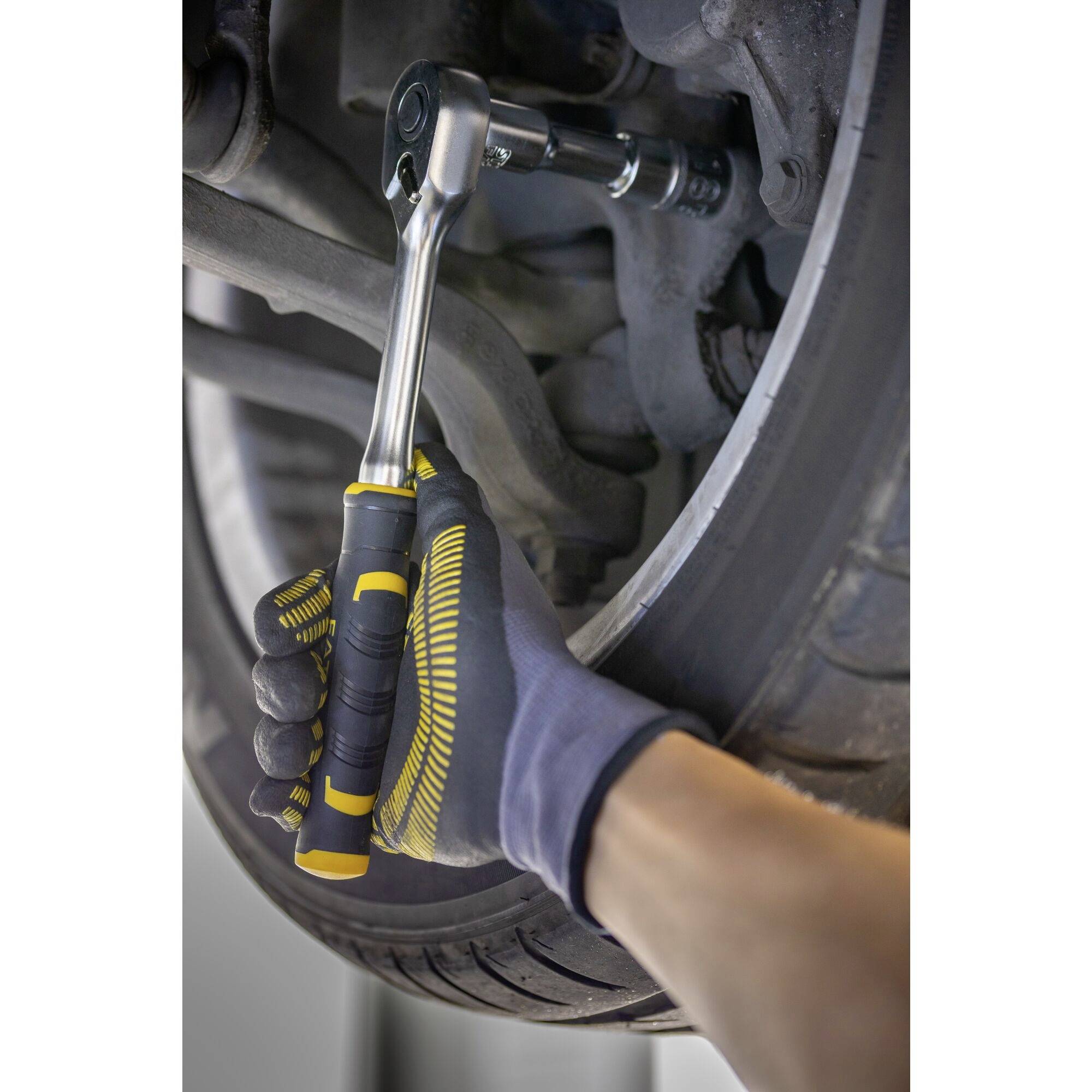 Ruka v černé rukavici používá ráčnu k uvolnění nebo utažení šroubu na pneumatice automobilu.