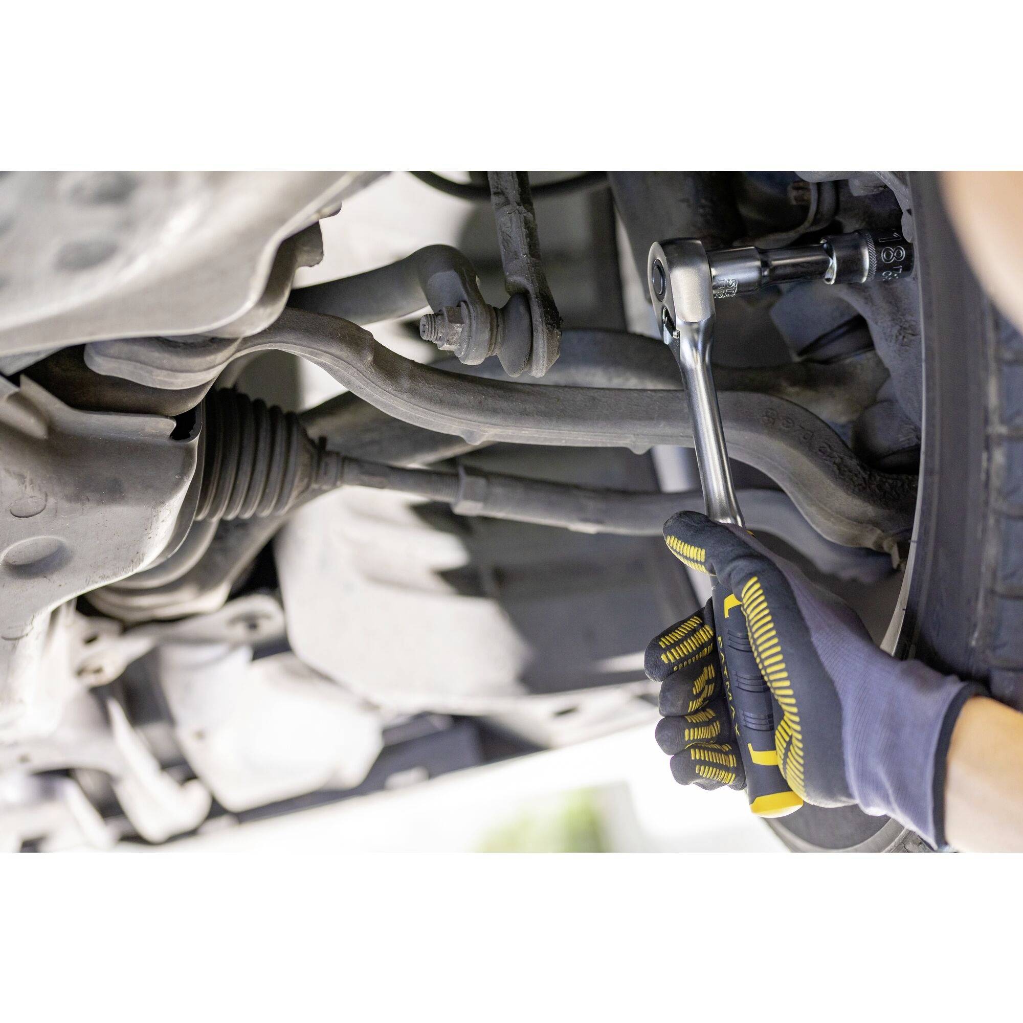 Mechanik v rukavicích opravuje součást automobilu pod vozidlem pomocí klíče.