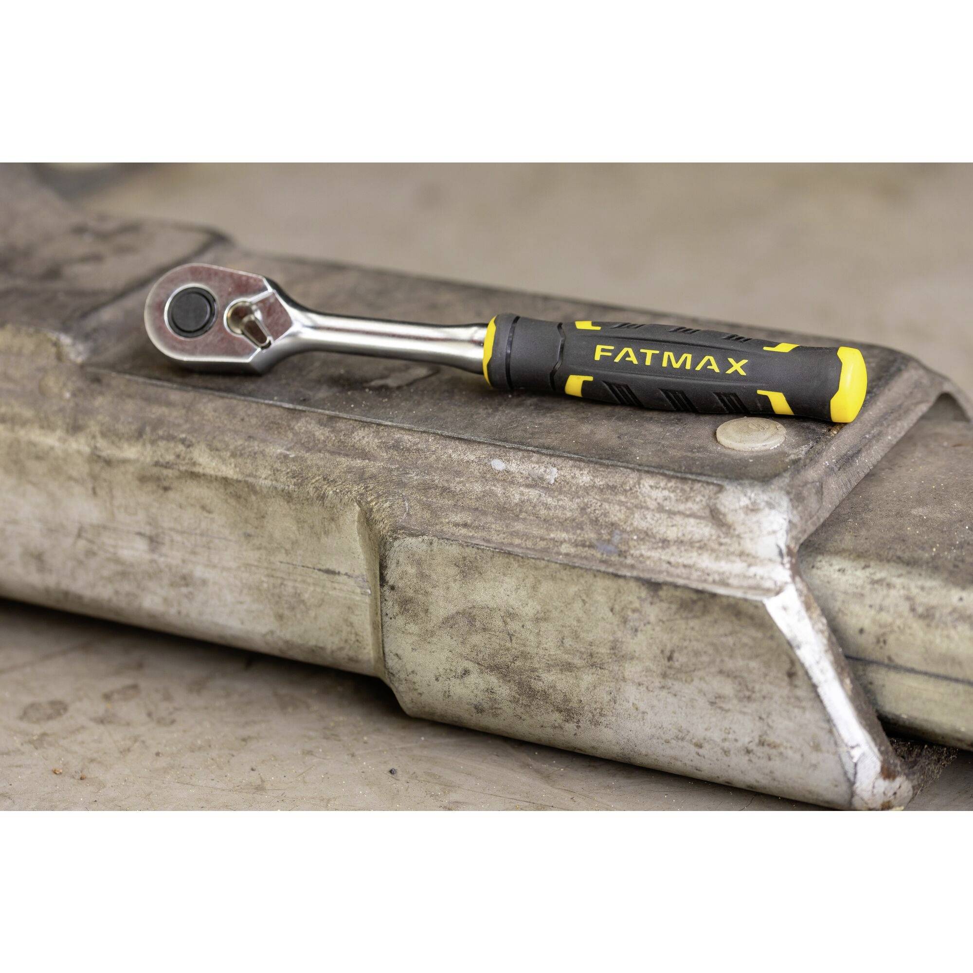 Francouzský klíč s žluto-černou rukojetí s nápisem "FATMAX" leží na hrubém kovovém povrchu.