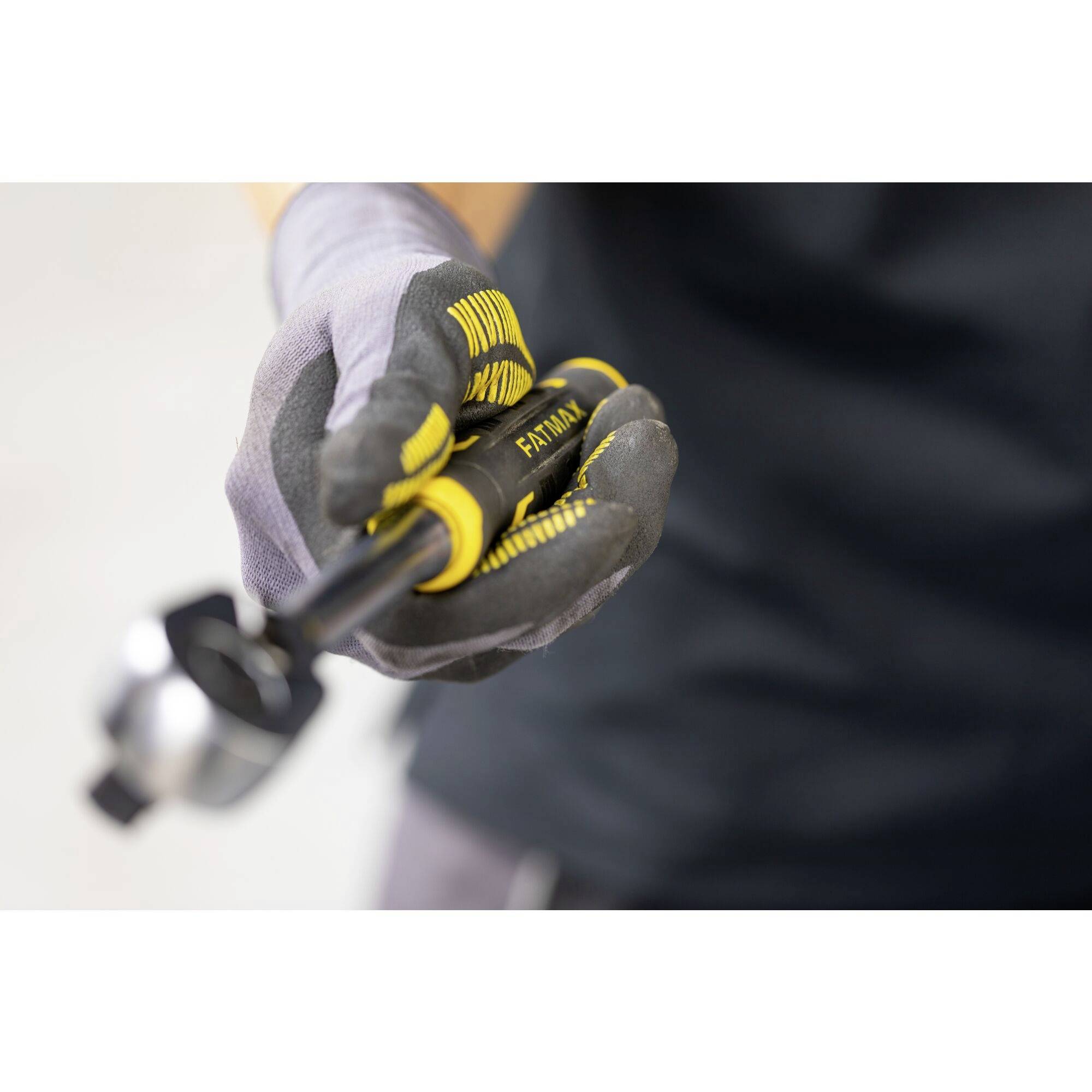 Osoba drží v rukavicích žluté a černé nářadí. Nářadí má nápis 'FATMAX'.