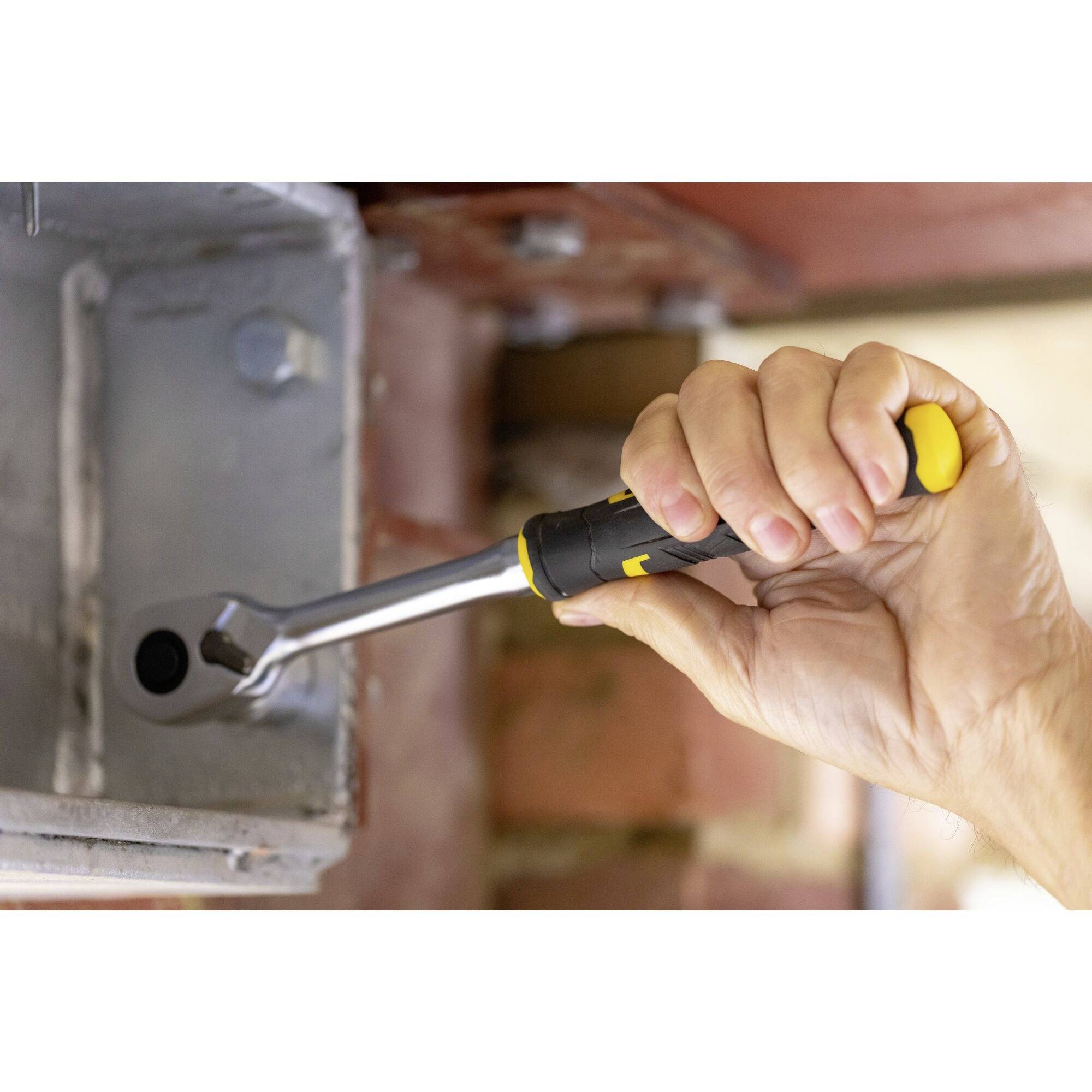 Ruka drží klíč, který pracuje na stříbrné kovové struktuře v popředí staveniště.