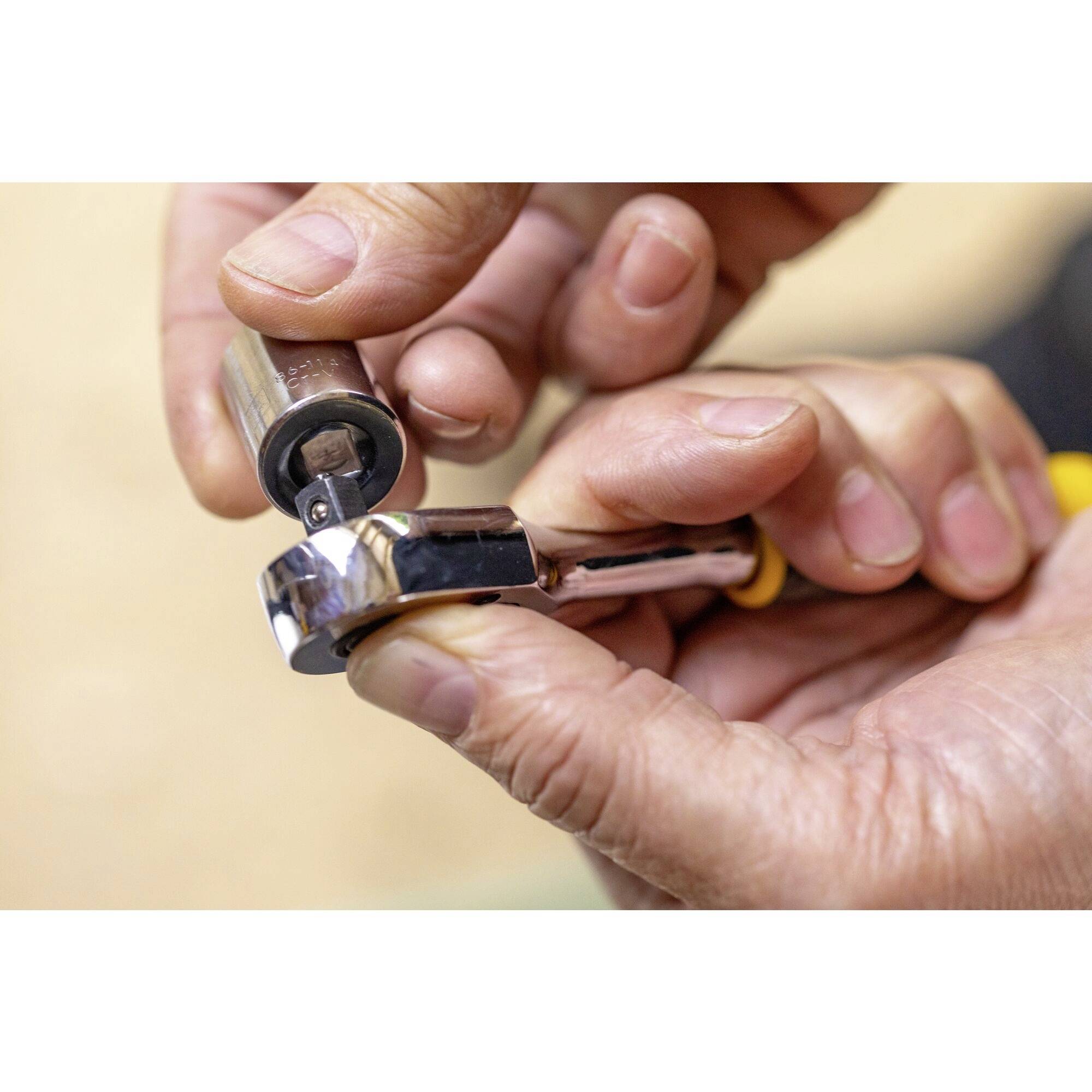 Někdo drží ráčnu a nasazuje nástrčný klíč. Ruce a nářadí jsou středem obrazu.