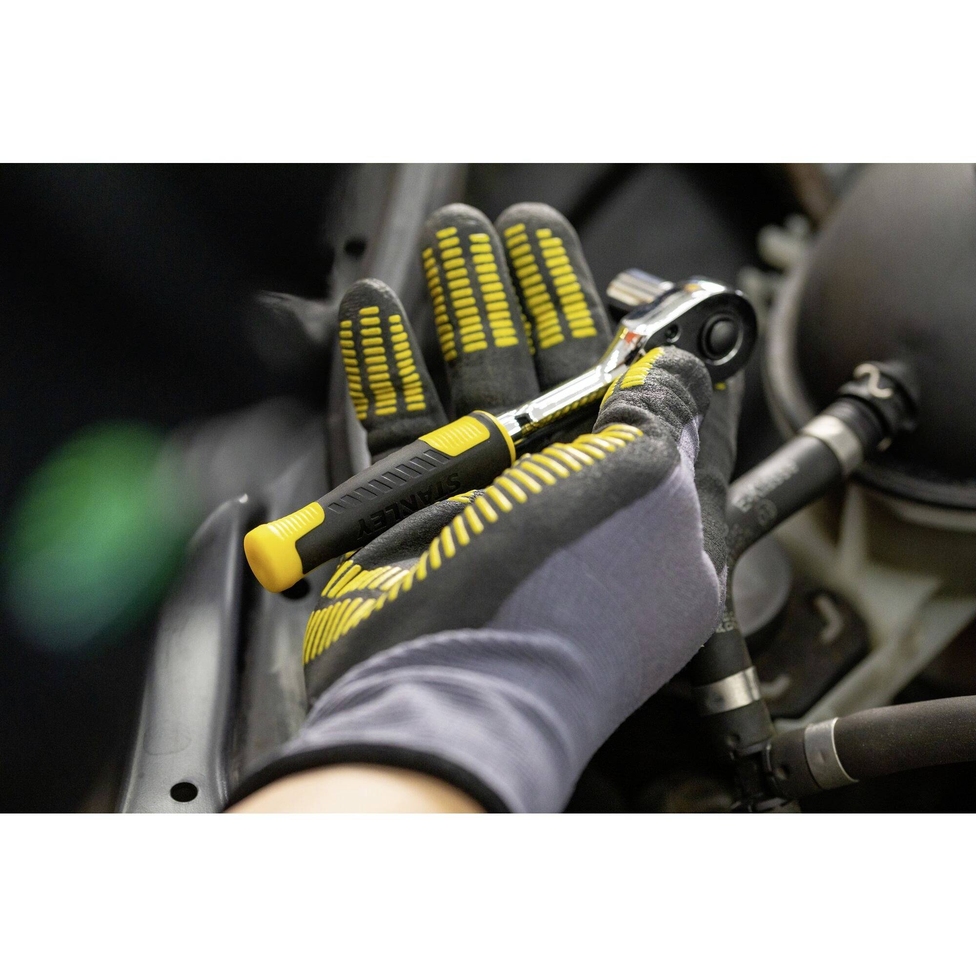 Osoba v ochranných rukavicích drží ráčnu a pracuje na motoru vozidla.