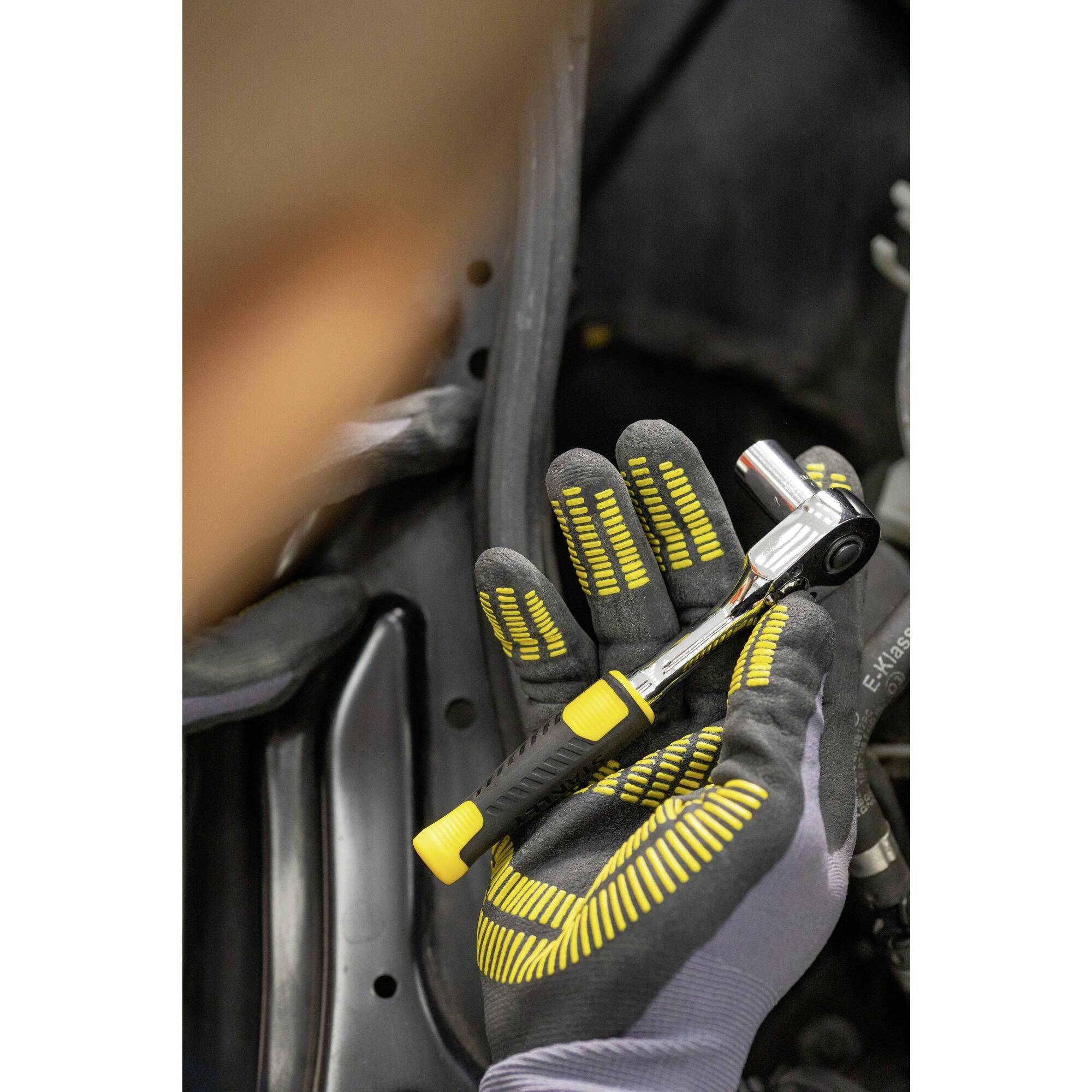 'Detailní záběr osoby držící ráčnu v autoservisu. V pozadí je vidět část motoru.'