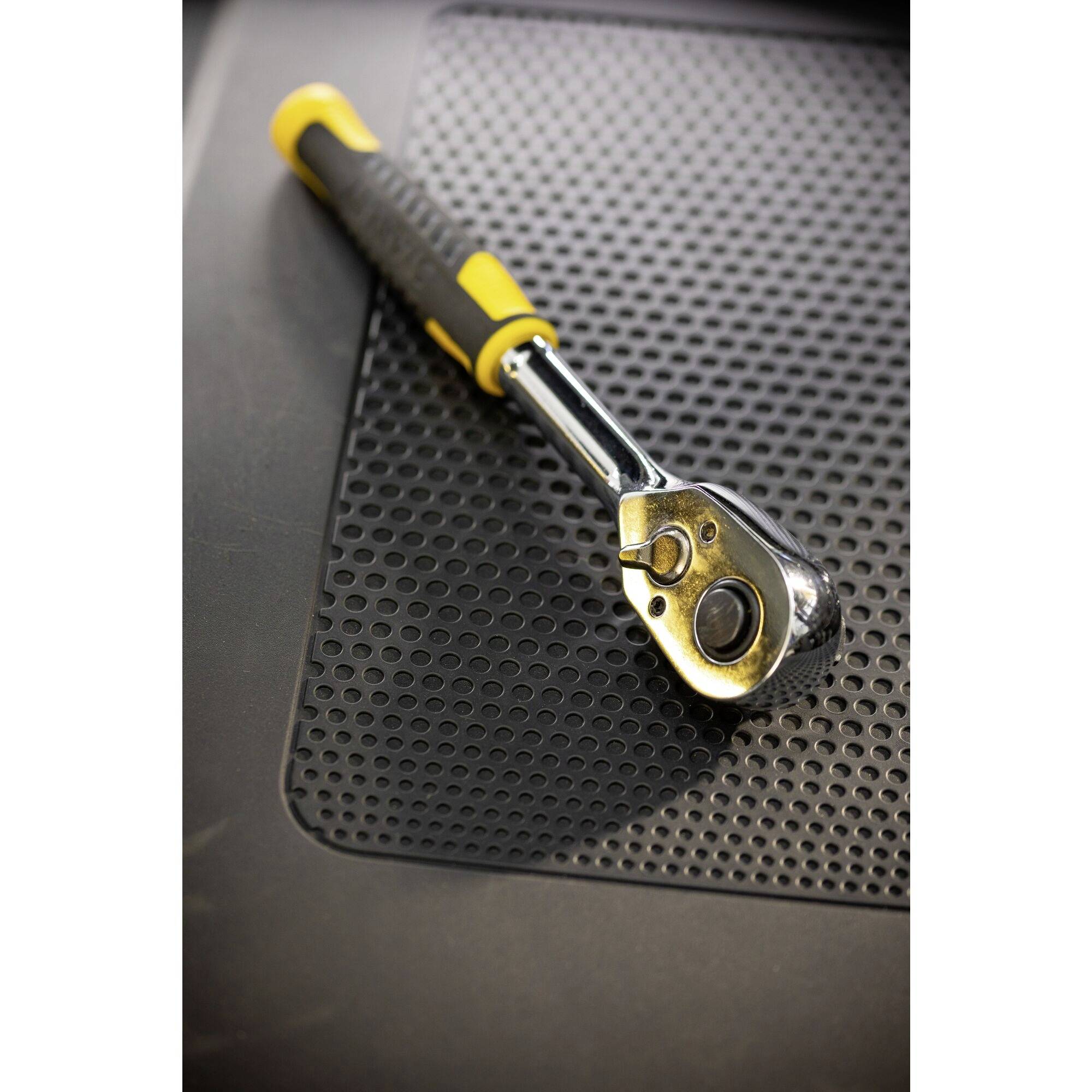 Nastavitelný klíč s žlutou rukojetí leží na černé vroubkované podložce.