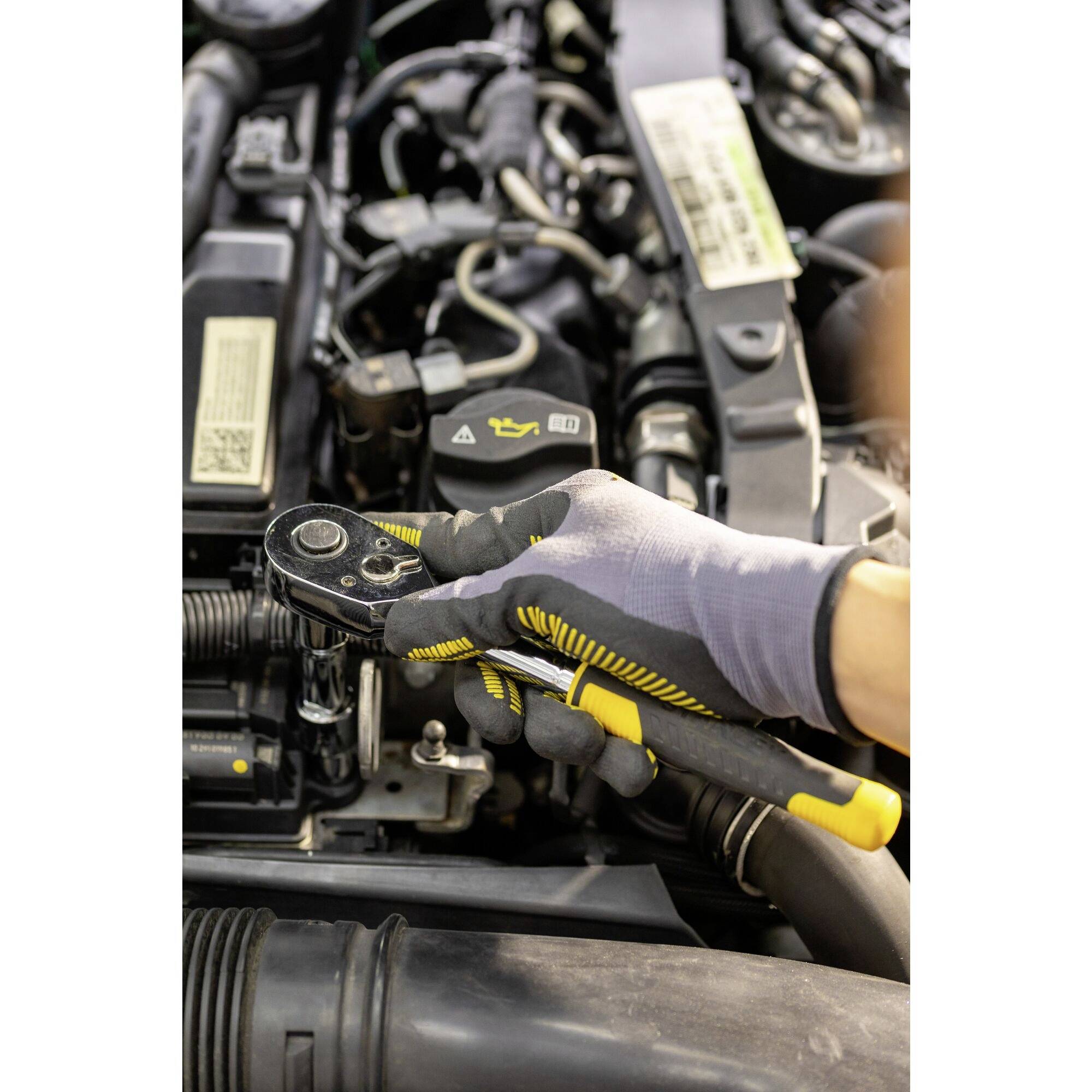 Osoba drží ráčnu v motorovém prostoru automobilu. V pozadí jsou viditelné různé díly motoru.