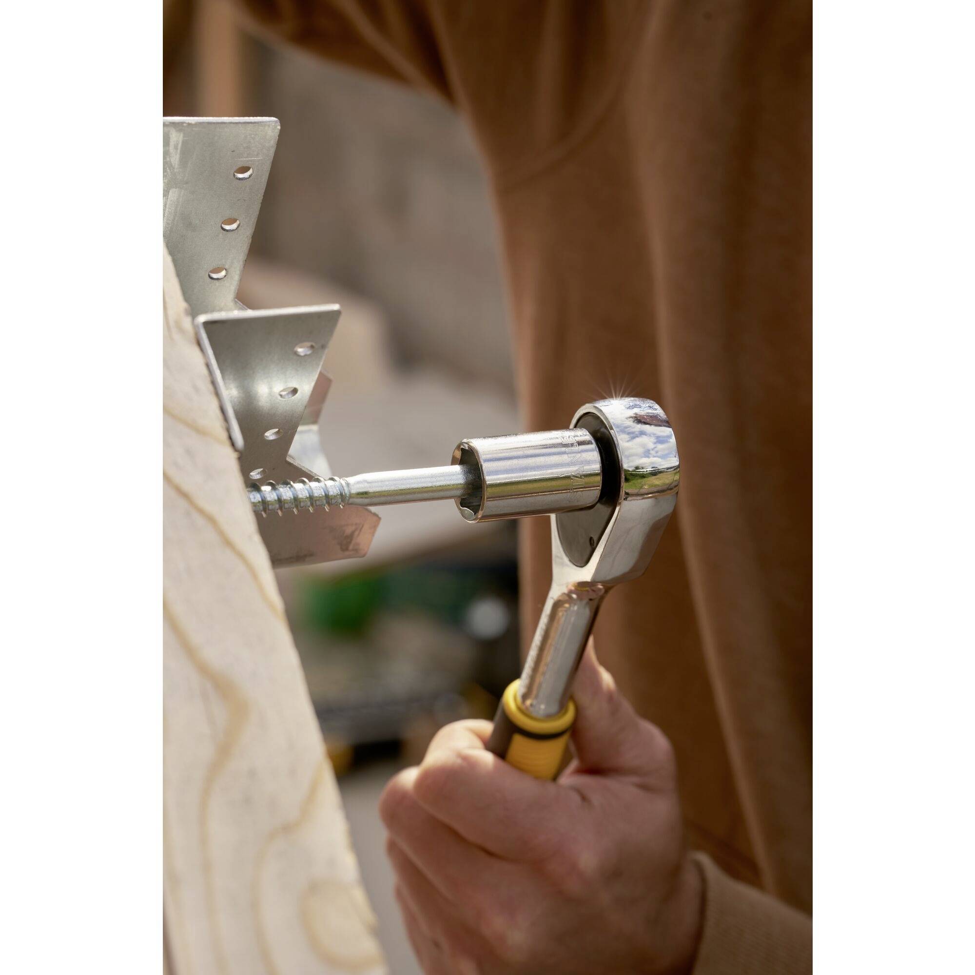 Osoba utahuje šroub klíčem, aby upevnila kovovou část na dřevěném dílu.