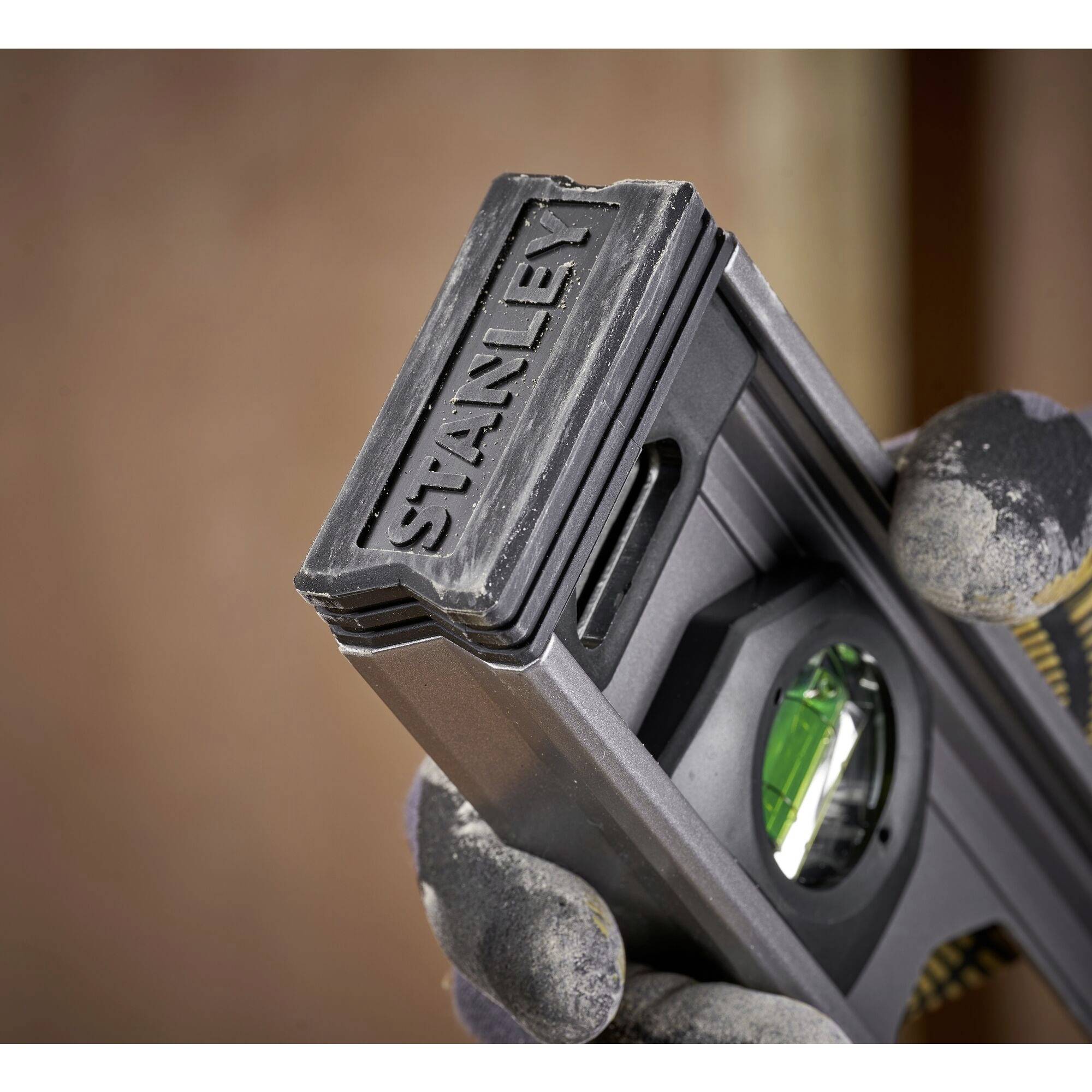 Ruka drží černou vodováhu se zelenou libelou, viditelná značka Stanley.