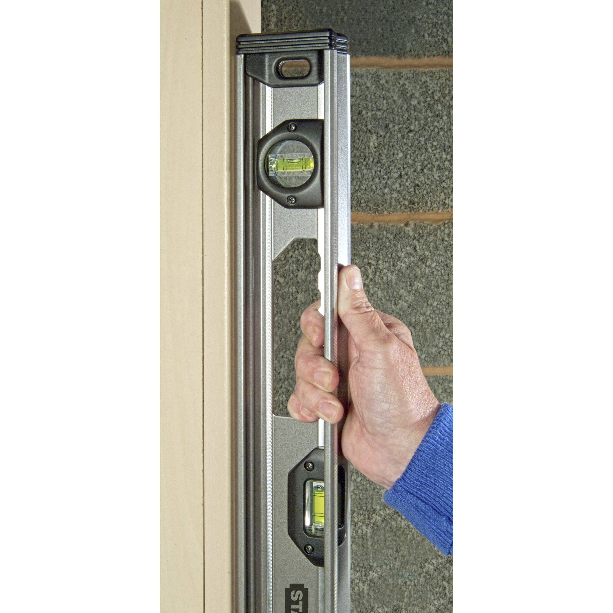 Osoba drží vodováhu, aby zkontrolovala svislost dřevěné stěny. Bublinka ukazuje dokonalé vyrovnání.