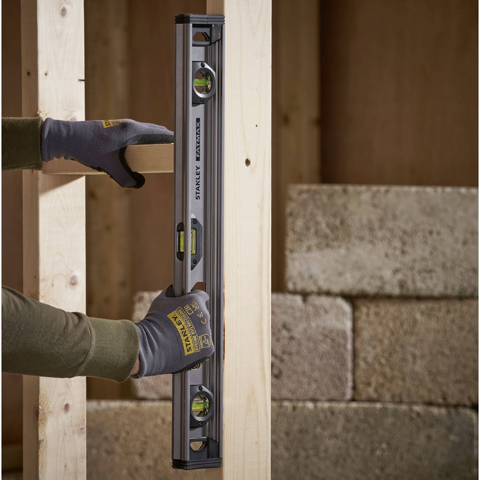 Jedna osoba přikládá vodováhu k dřevěnému trámu, aby zkontrolovala svislost při stavbě budovy.