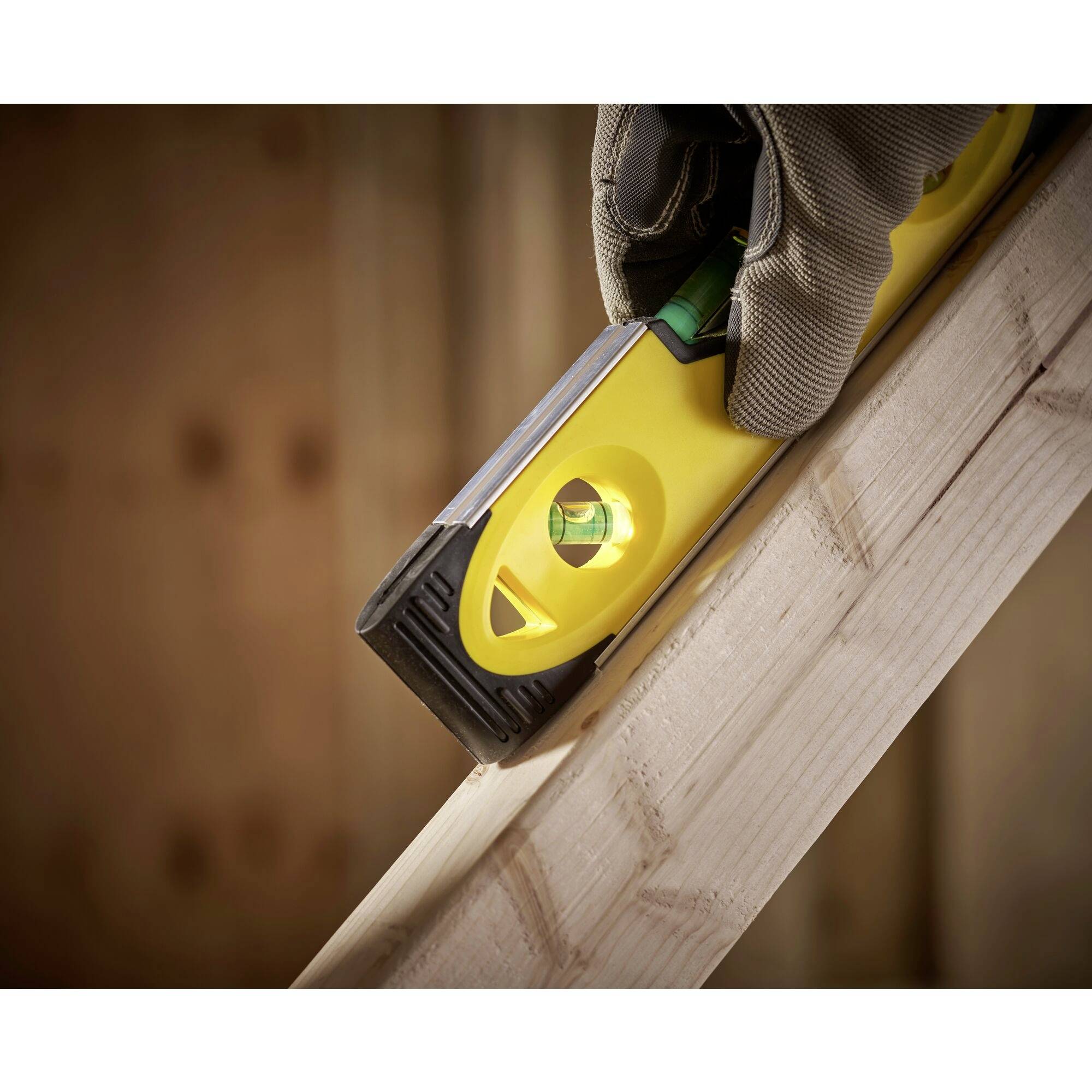 Ruka v pracovní rukavici drží žlutou vodní váhu na šikmém dřevěném prkně, aby zkontrolovala sklon.