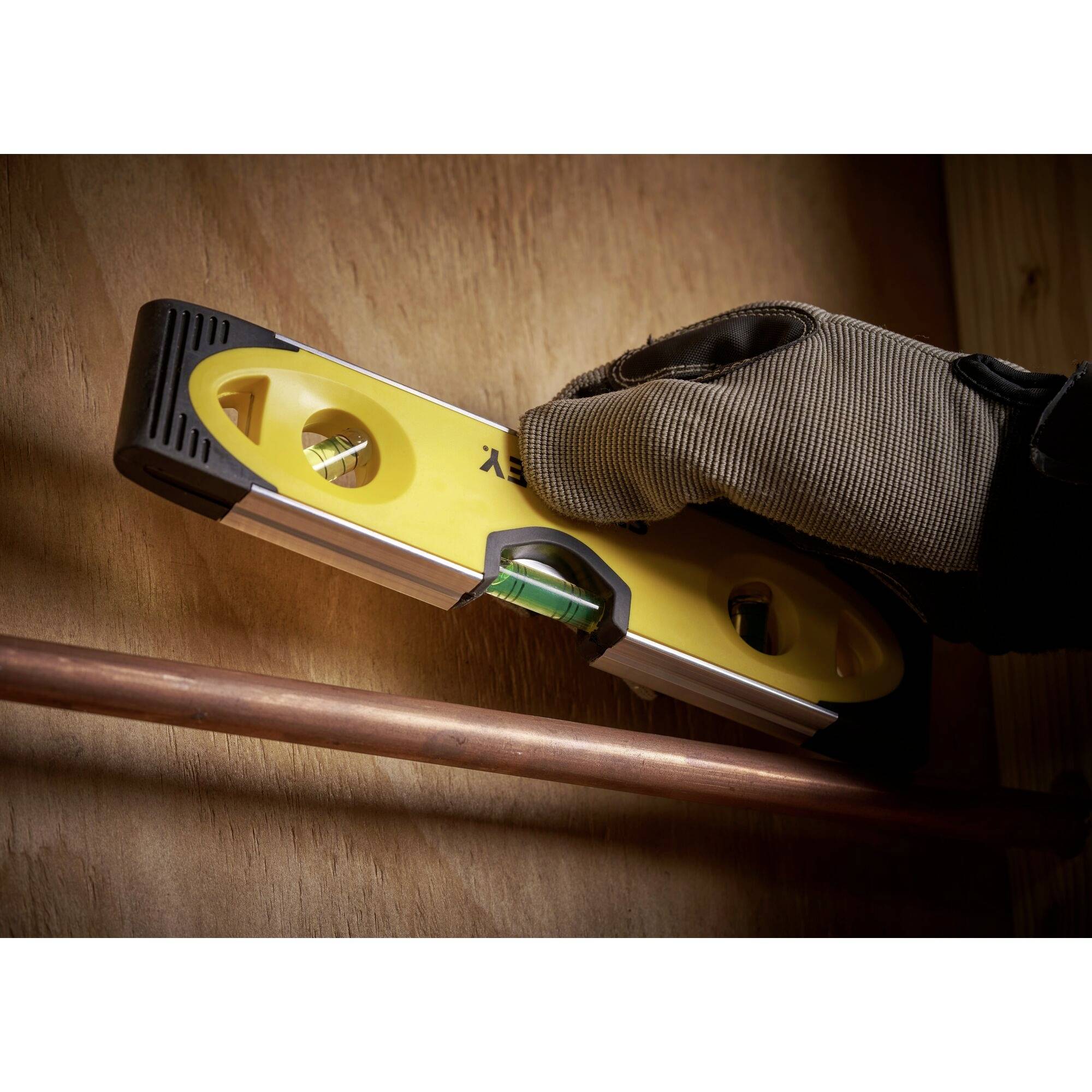 Ruka v rukavici drží vodováhu u měděné trubky, aby zkontrolovala vyrovnání.