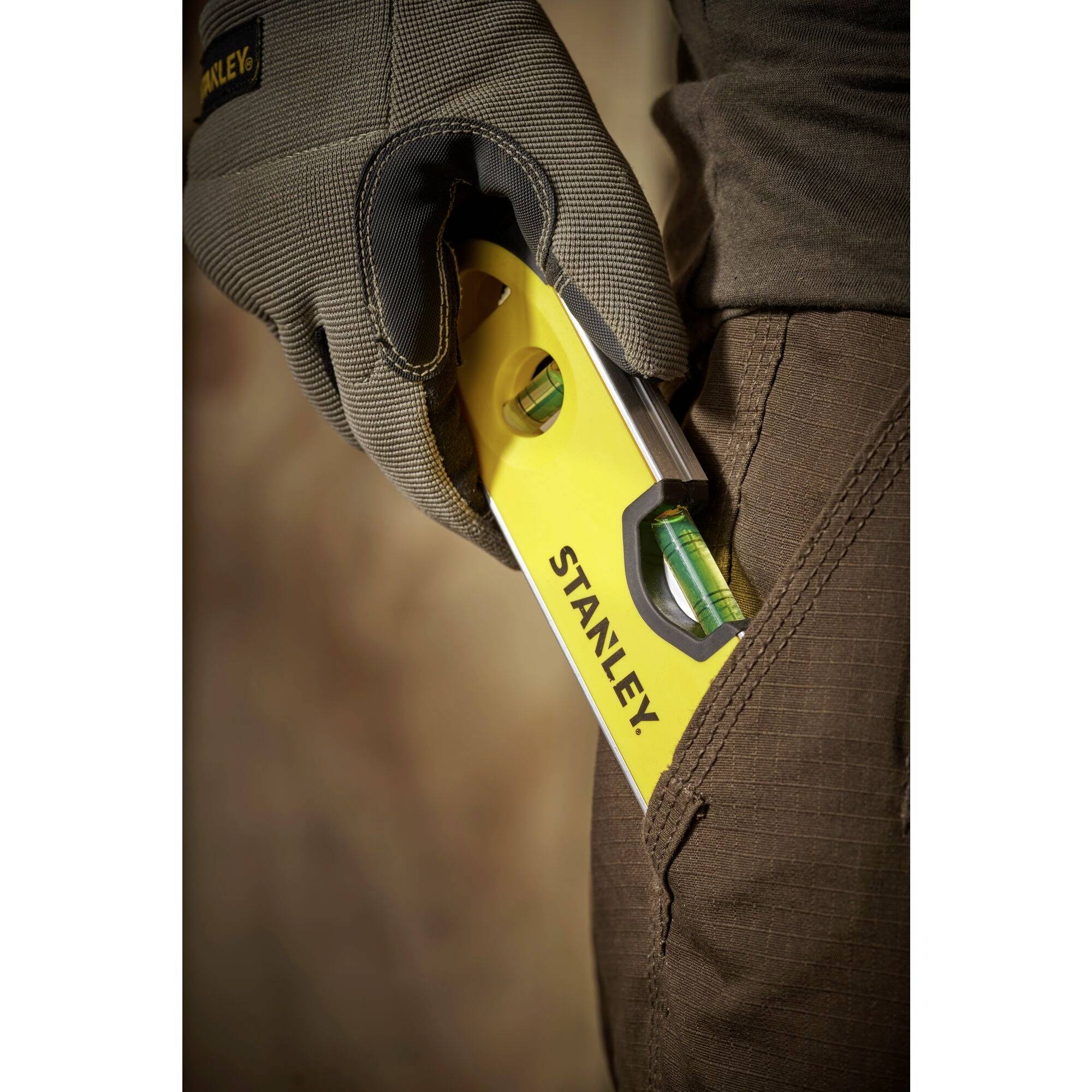 Osoba drží žlutou vodní váhu značky STANLEY v ruce. Vodní váha ukazuje přesné vodorovné vyrovnání.