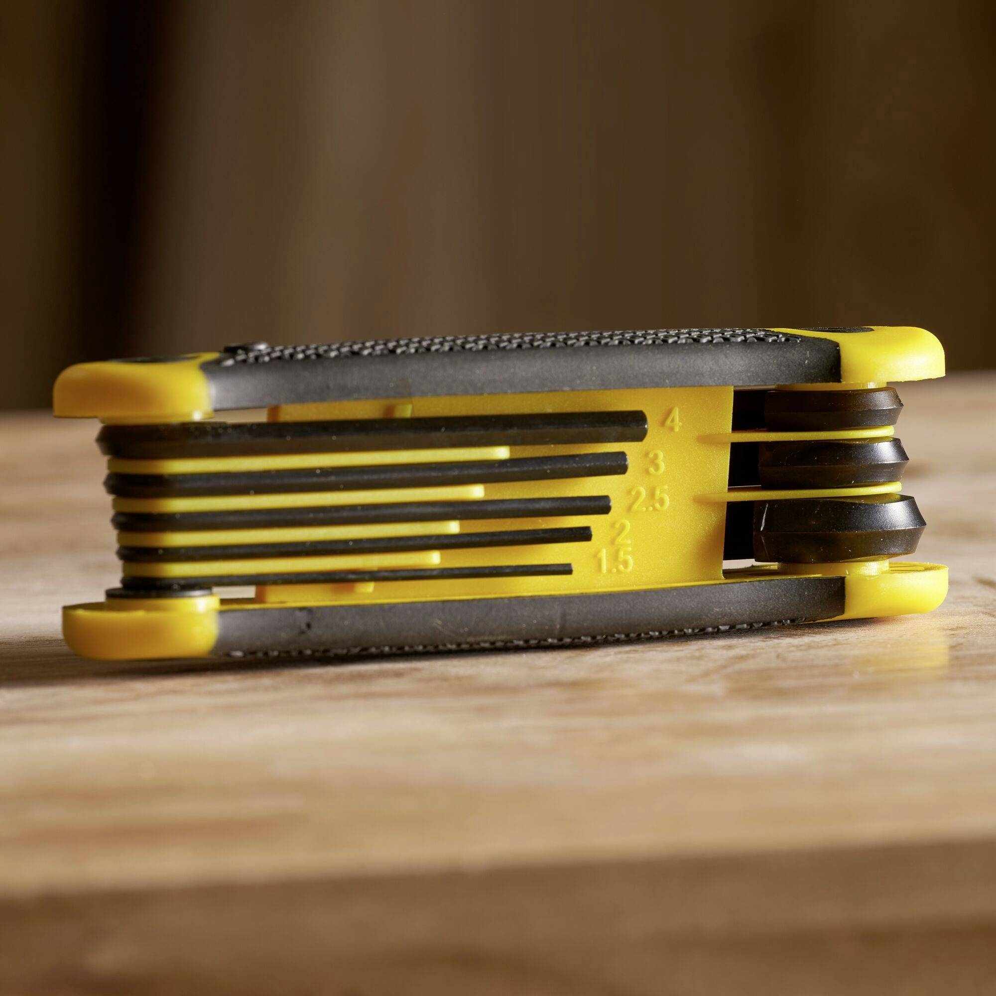 Žlutý a černý nástroj na krájení potravin na dřevěném podkladu s nastavitelnými čepelemi pro různou tloušťku.