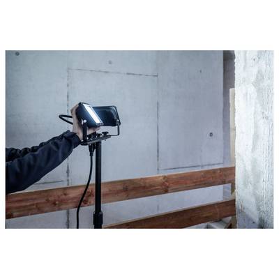 Osoba upravuje připevněnou LED pracovní lampu na stativu v nedokončené místnosti s odkrytými stěnami a dřevěným ztužením.