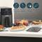 Horkovzdušná fritéza na kuchyňské lince, obklopená talíři s chuťovkami a zeleninou. Ikony znázorňují výhody: méně oleje, snadné čištění.