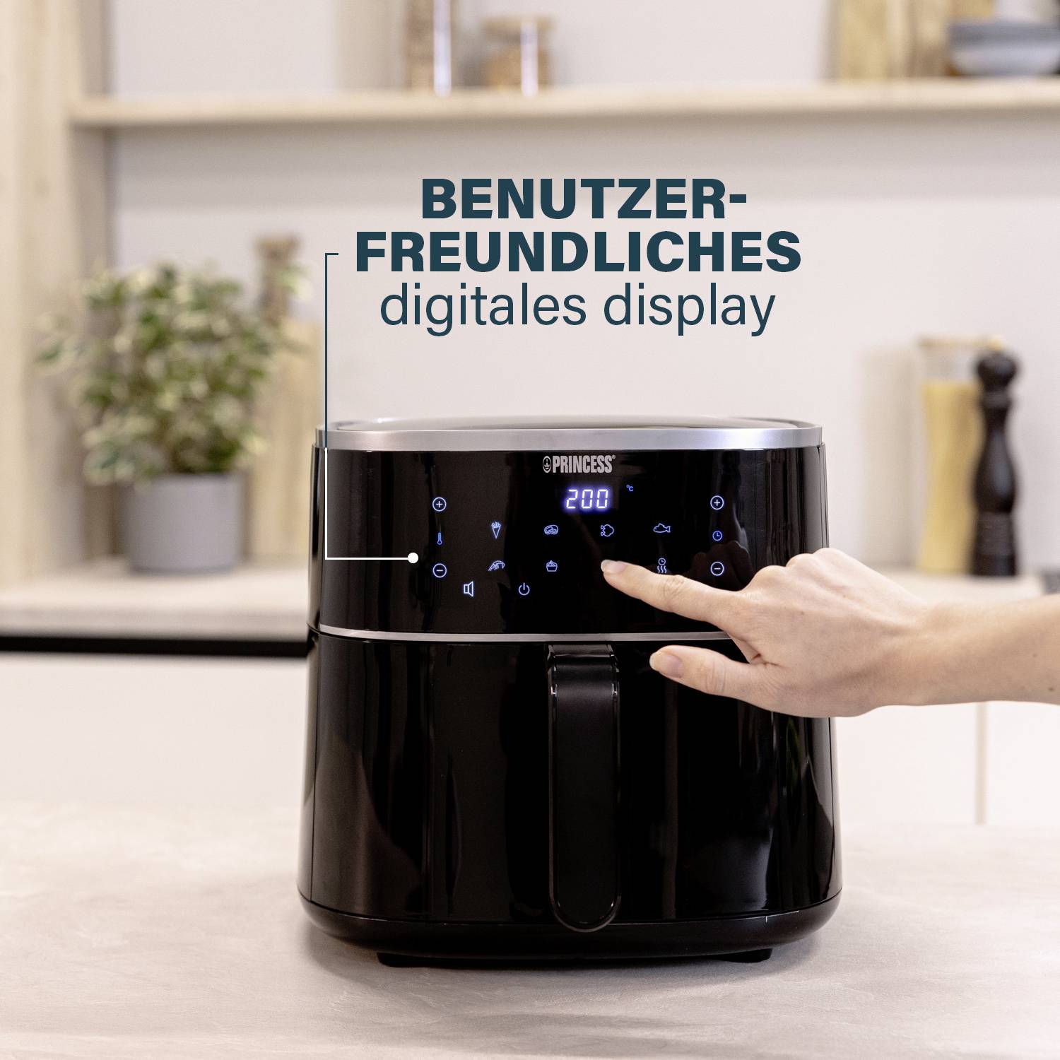Ruka ovládá digitální displej na černé horkovzdušné fritéze. V pozadí je vidět kuchyňská pracovní deska.