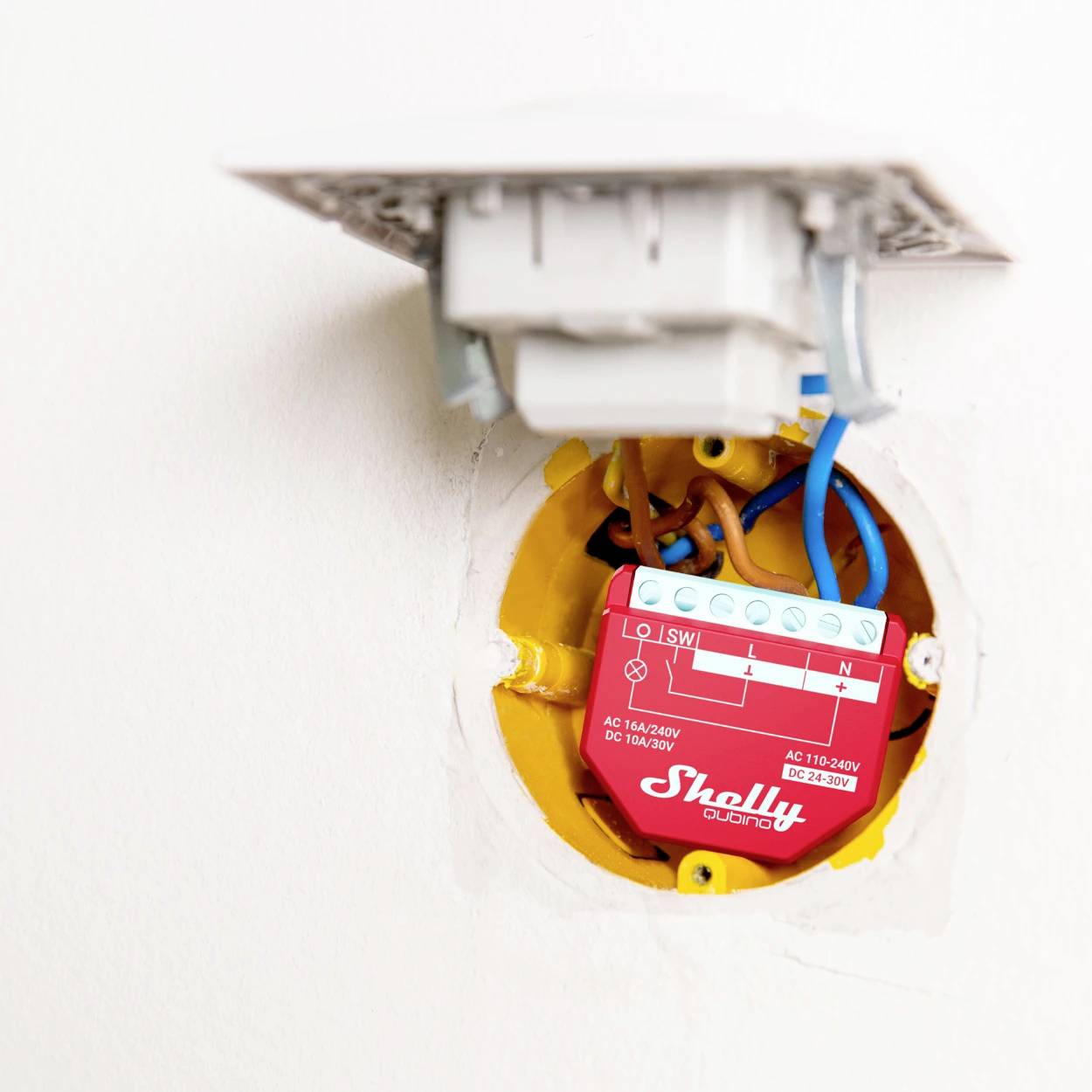 Otevřená elektrická rozvodná skříň na zdi ukazuje červený elektrický modul s modrými a hnědými vodiči, určený k ovládání přístrojů.