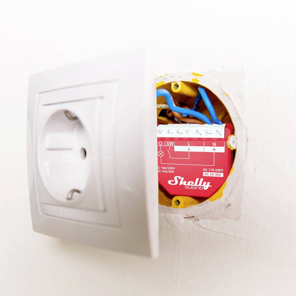 Částečně otevřená zásuvka odhaluje malé vestavěné červené elektrické zařízení značky 'Shelly'.