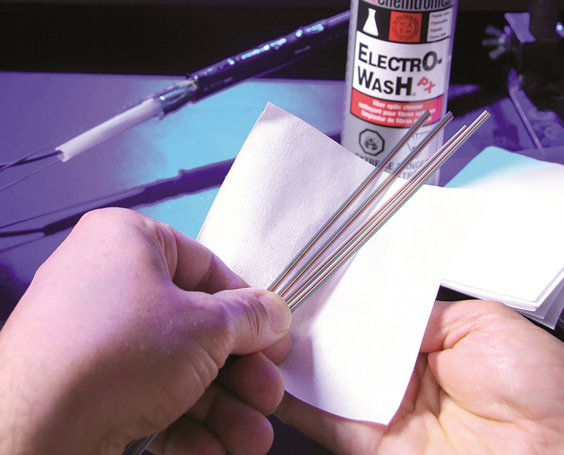 Dvě ruce čistí kovové tyče bílým hadříkem. V pozadí stojí láhev s nápisem 'Electro-Wash'.