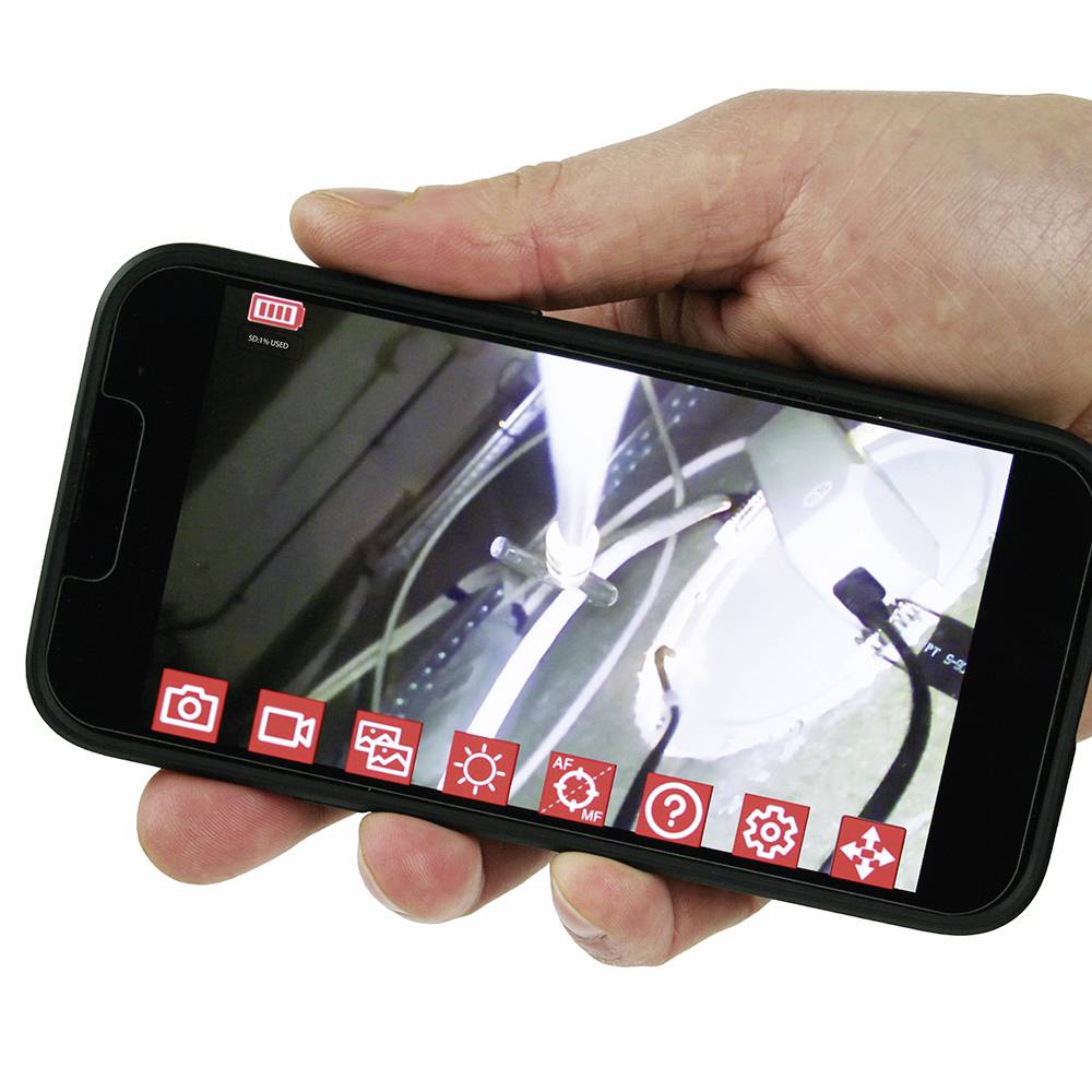 Jedna ruka drží smartphone, který zobrazuje živý videosnímek technického stroje s několika symboly na displeji.
