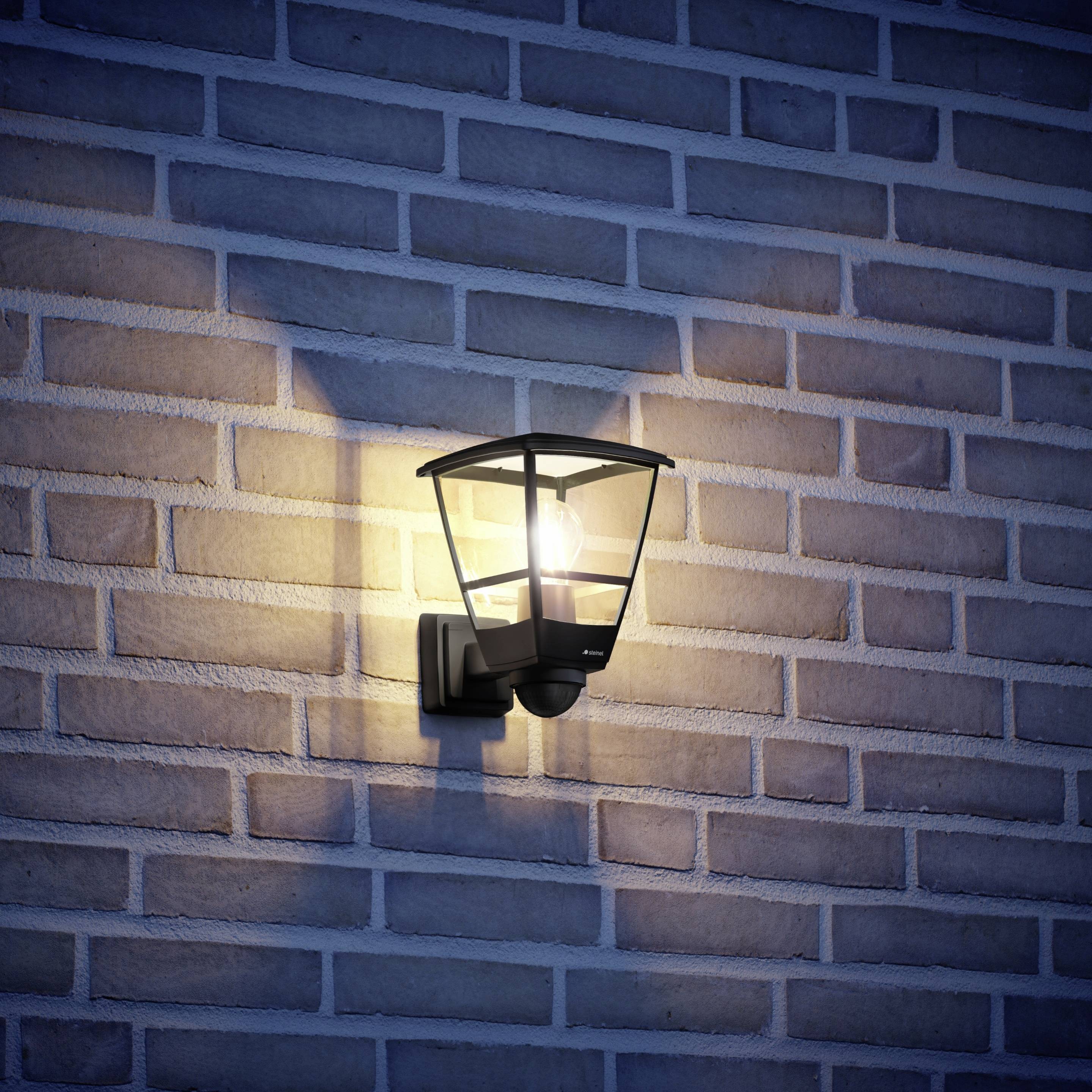 Venkovní lampa na cihlové zdi osvětlená ve tmě vytváří teplý světelný odlesk na stěně.