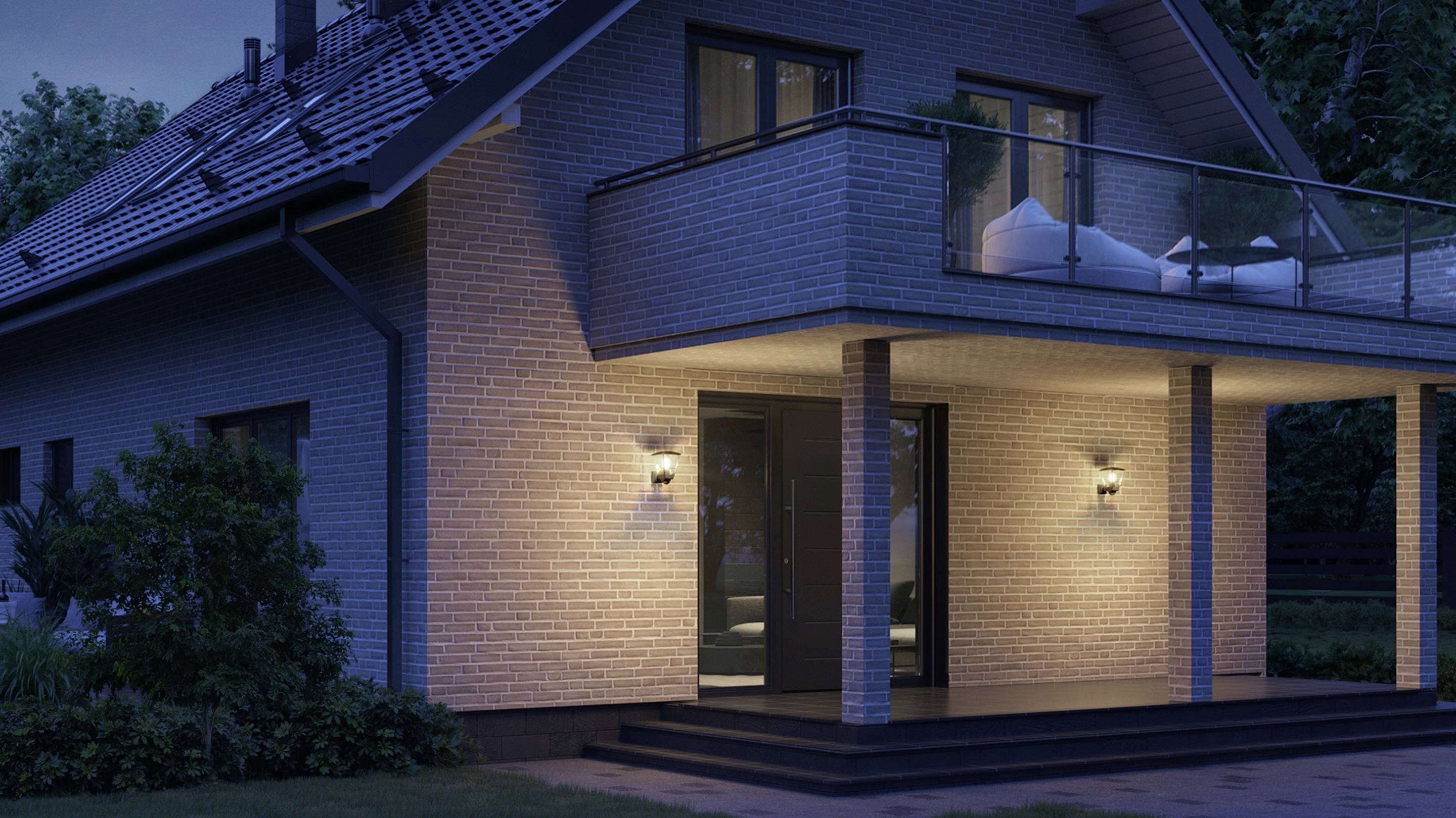 Moderní rodinný dům v noci, osvětlený venkovními lampami, s balkónem a šikmou střechou, obklopený stromy.