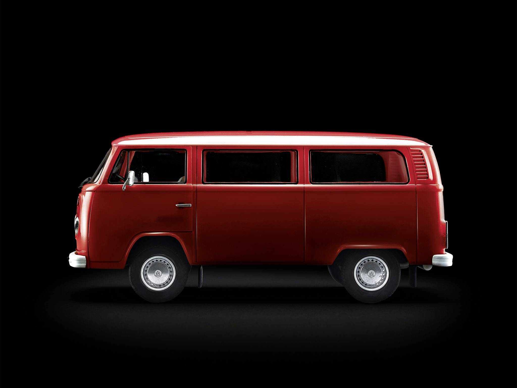 Červený autobus VW z modelové řady 70. let, pohled z boku na černém pozadí.