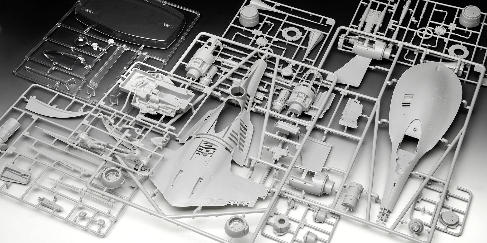 Plastikový modelářský kit vesmírné lodi na stole, díly předřazené. Obsahuje trup, křídla a motory na vtokových rámečcích.