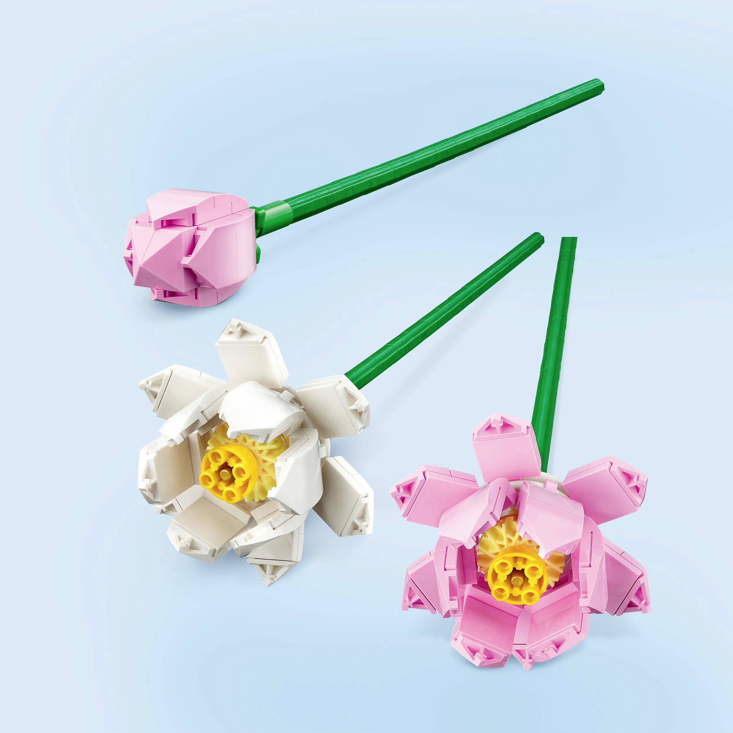 Tři LEGO květiny s dlouhými zelenými stonky. Jedna bílá, jedna růžová a jedna purpurová květina leží na světle modrém pozadí.