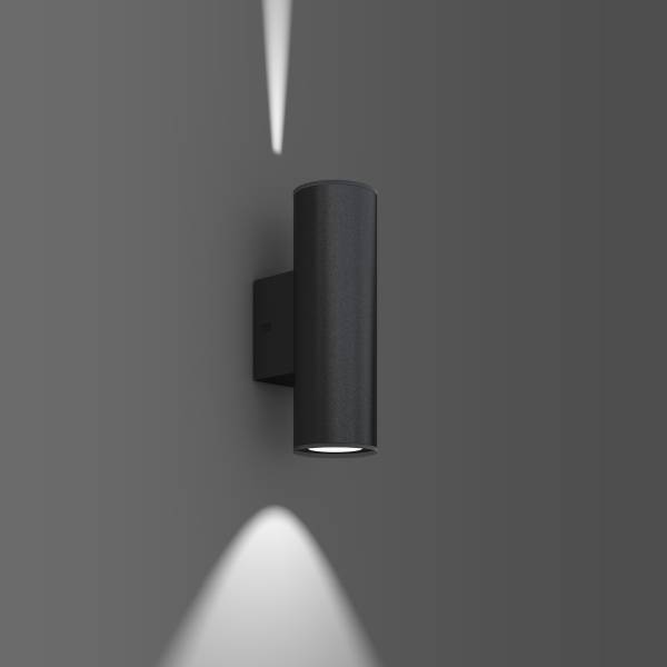 Černá moderní nástěnná lampa vyzařuje světlo nahoru a dolů na šedém pozadí.