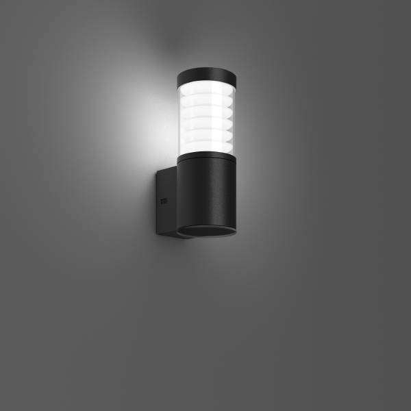 Nástěnná lampa s moderním designem, černým tělem a kulatým, vroubkovaným stínidlem, které rozptyluje tlumené světlo.
