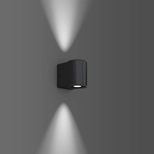 Černá nástěnná lampa vyzařuje světlo nahoru a dolů na šedou stěnu a vytváří dva kuželovité světelné paprsky.