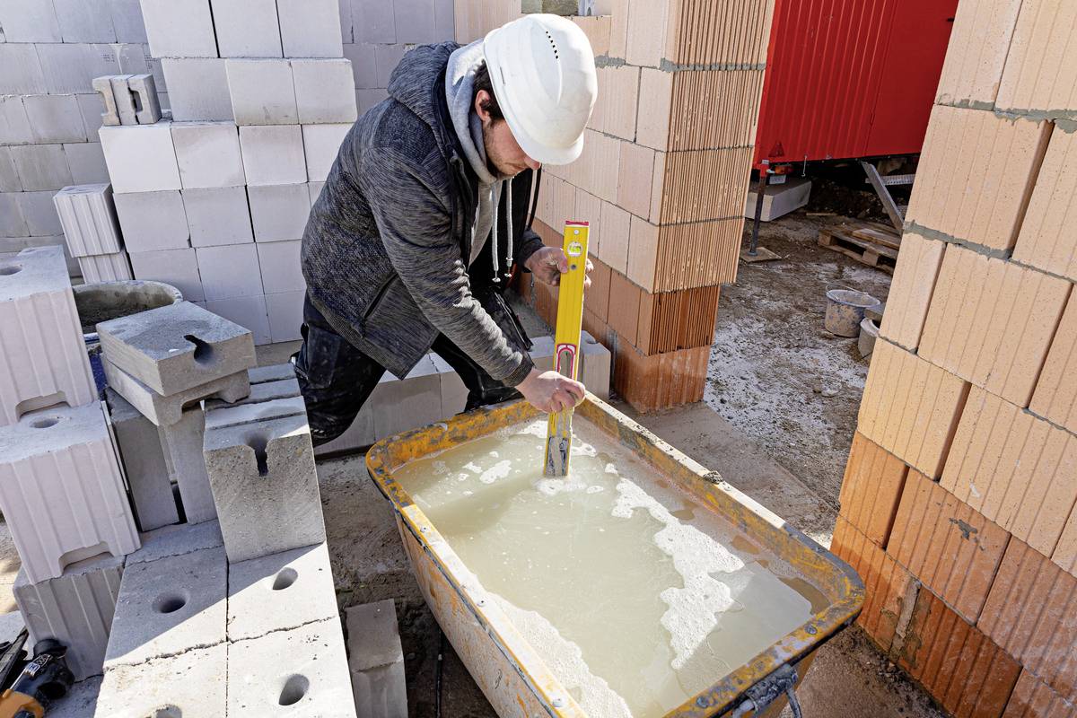 Dělník v ochranném oděvu míchá maltu v nádobě na staveništi obklopeném cihlovou zdí.