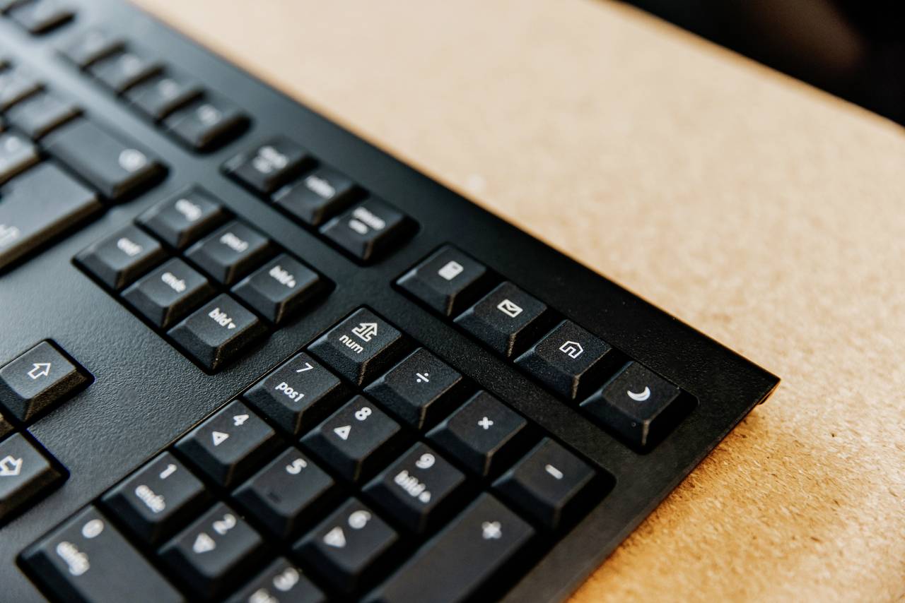 Počítačová klávesnice zaměřená na speciální klávesy jako 'E-mail' a 'Spánek'. Klávesy jsou černé s bílými symboly na světlém stole.