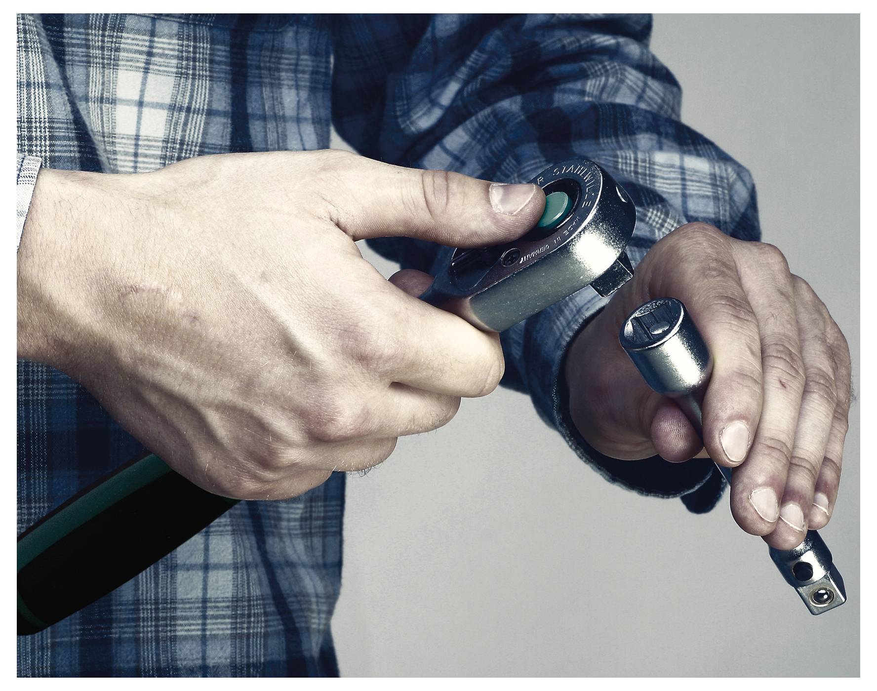 Osoba v kostkované košili připevňuje zásuvku k ráčnému klíči a zaměřuje se na přesnost a mechanickou práci.