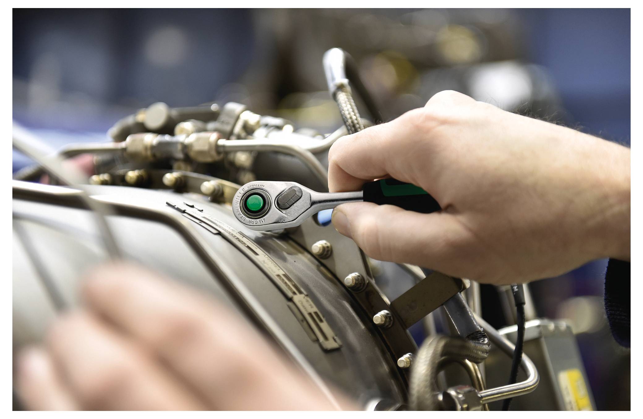 Osoba používá klíč k nastavení strojů a zaměřuje se na přesné vyrovnání. Prostředí naznačuje průmyslové nebo dílnové prostředí.