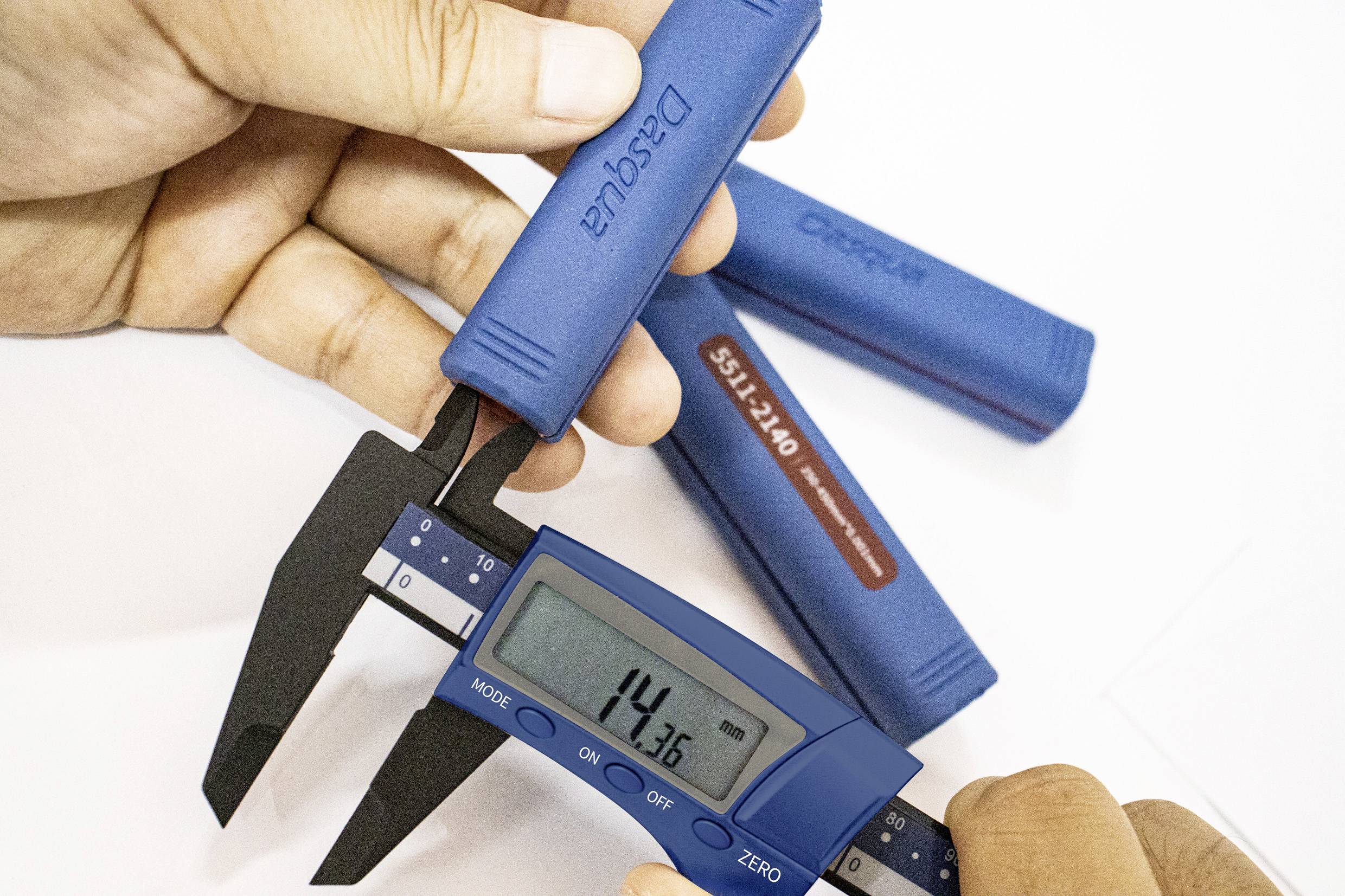 Digitální posuvné měřidlo měří objekt s hodnotou 14,36 mm, držené dvěma rukama.