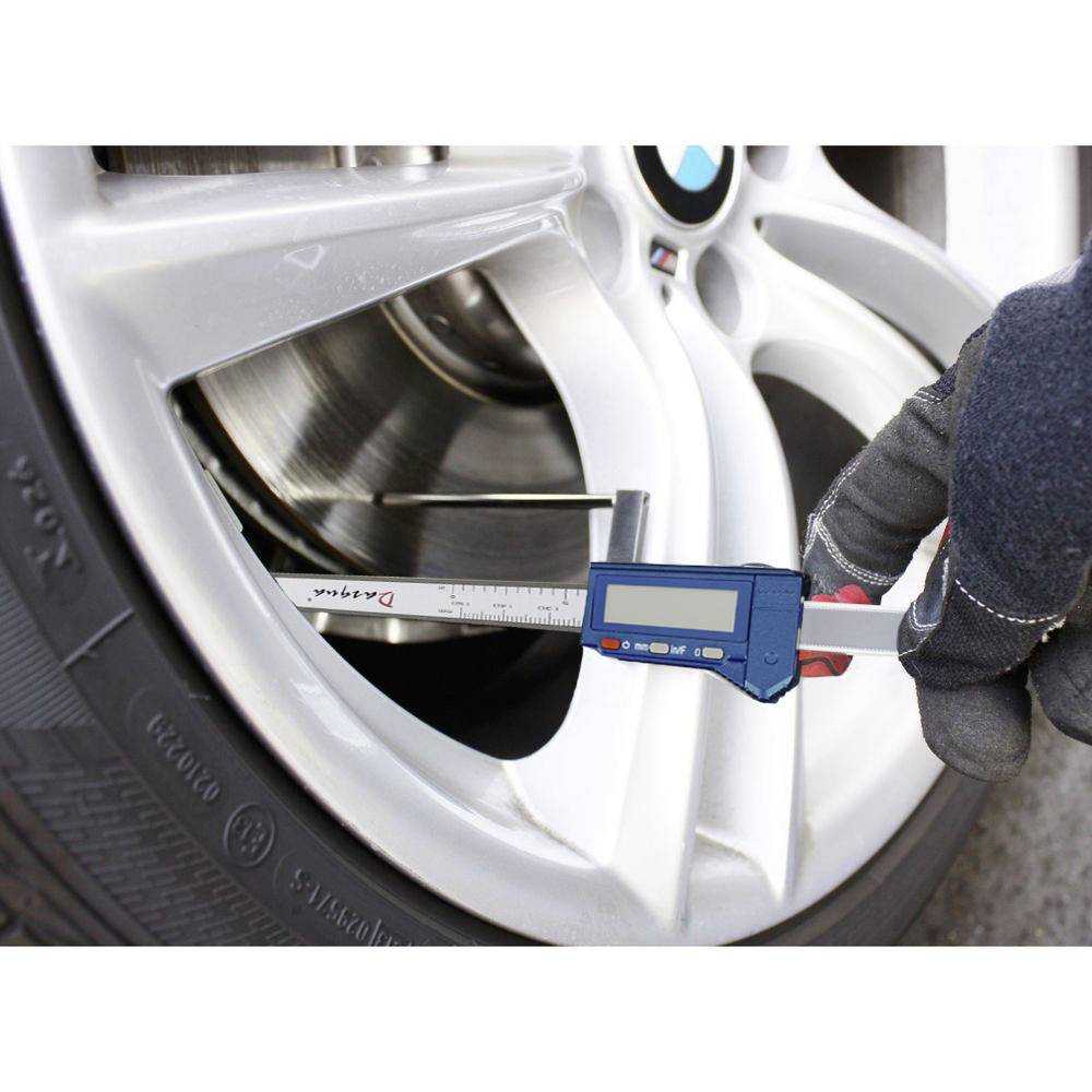 Ruka v rukavici měří tloušťku brzdového kotouče na pneumatice automobilu digitálním posuvným měřítkem za účelem kontroly opotřebení.