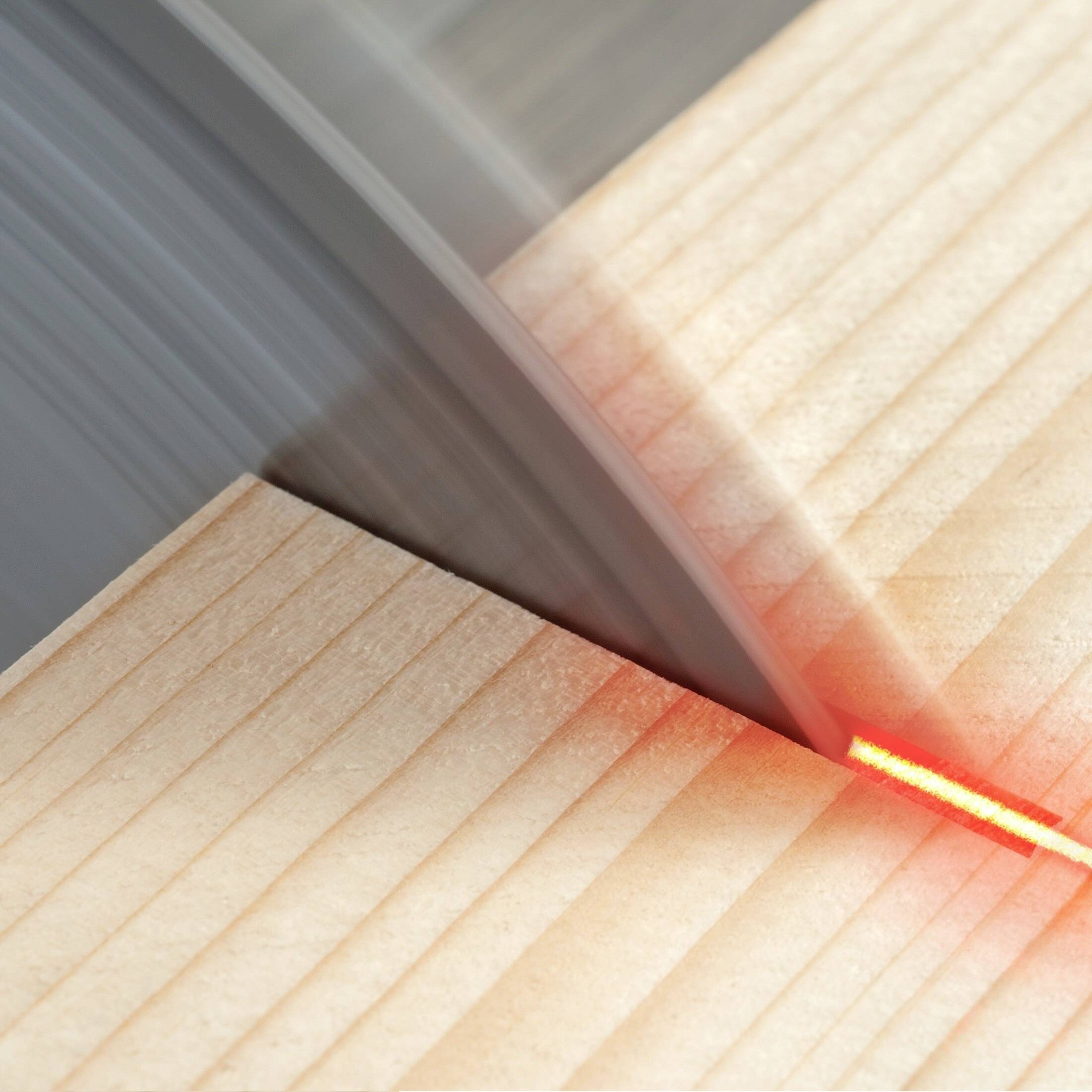 Dřevěná deska je přesně rozřízána kotoučovou pilou, což je patrné z rotujícího pilového kotouče a červených laserových vodicích čar.