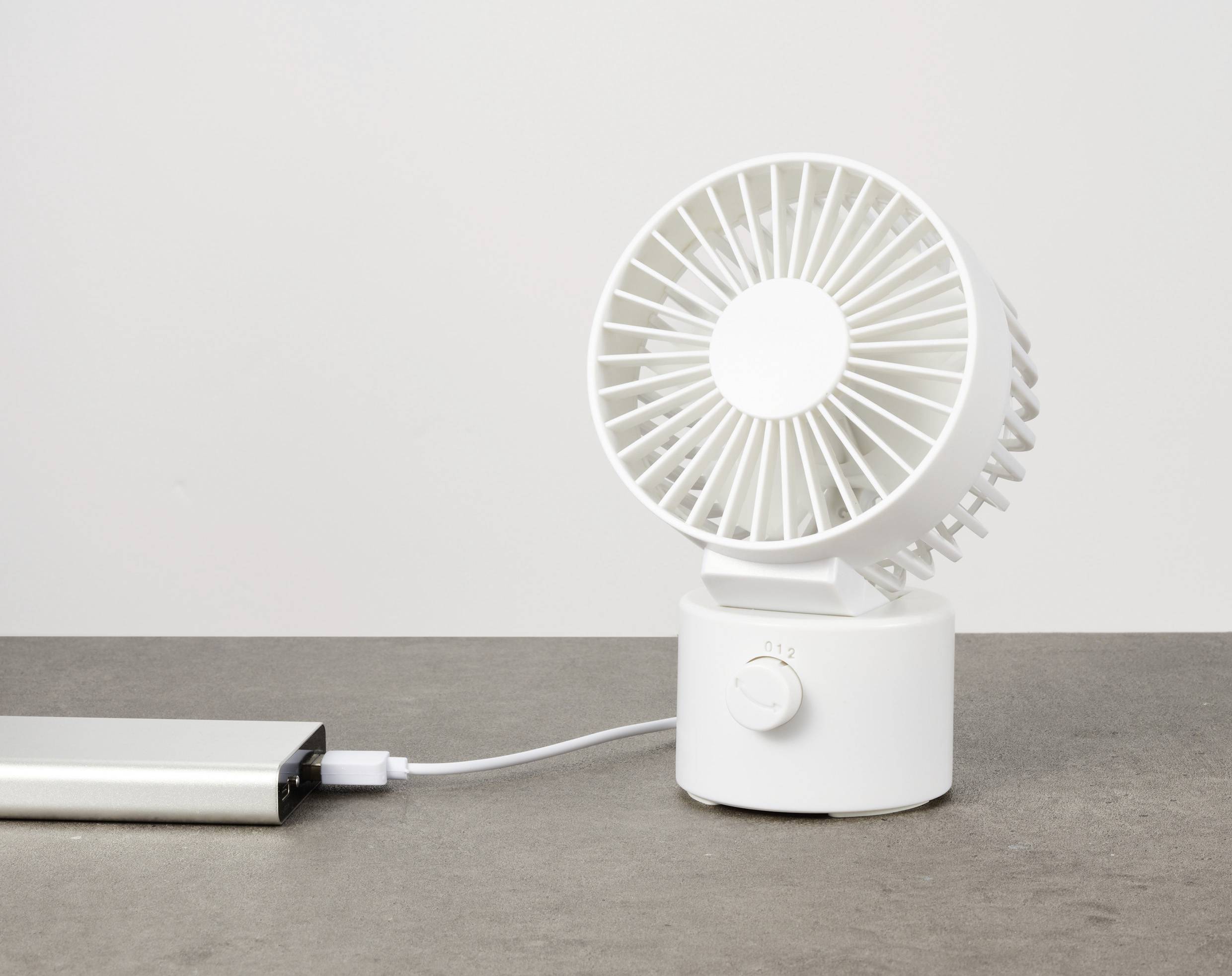 Bílý USB ventilátor na šedém povrchu, připojený k powerbance.