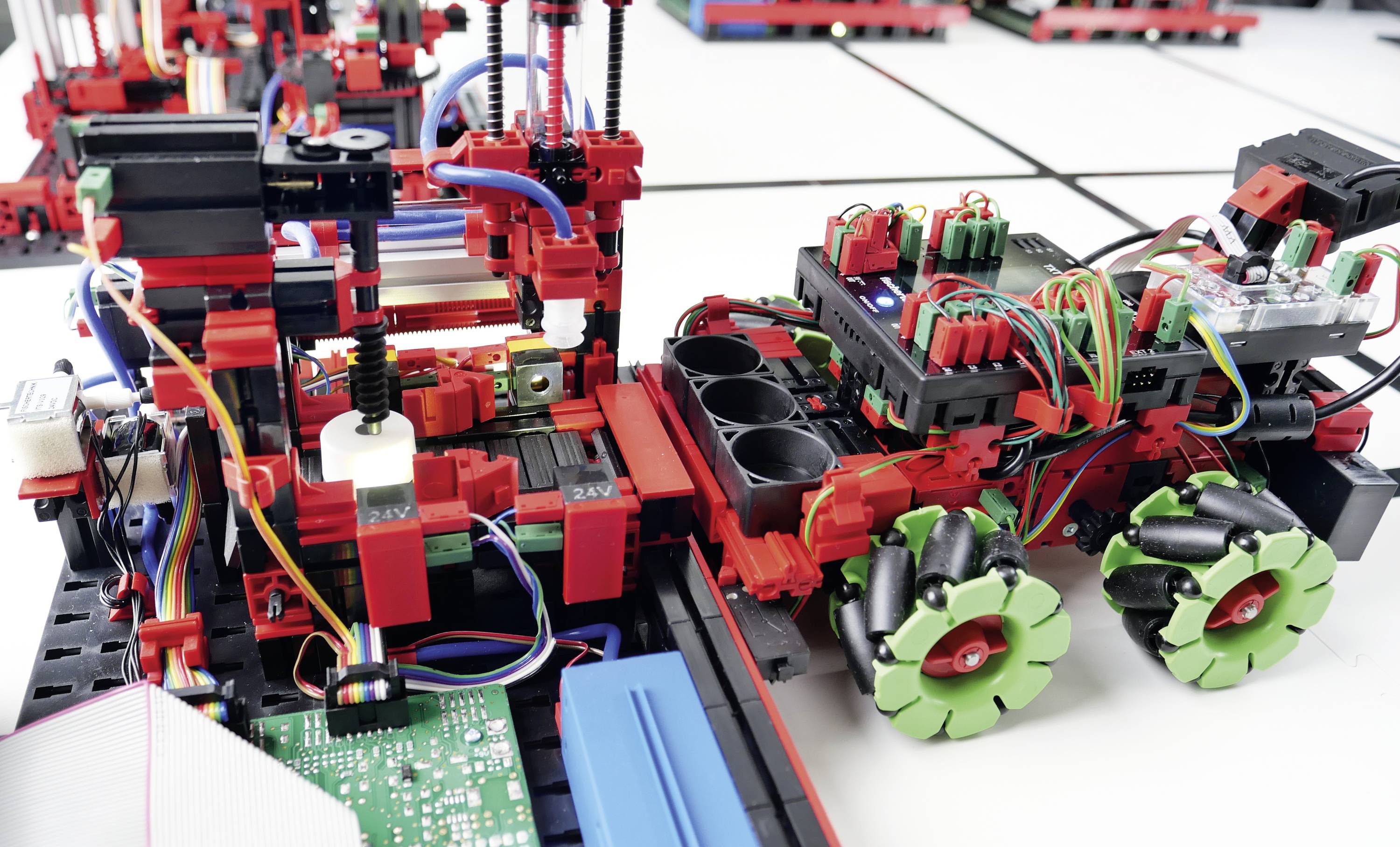 Průmysloví roboti v červené a černé barvě na laboratorním stole, vybaveni elektronikou, senzory a propojenými moduly.