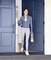 Žena ve sportovním oblečení stojí s úsměvem u otevřených dveří, v rukách drží podložku na jógu a láhev s vodou.