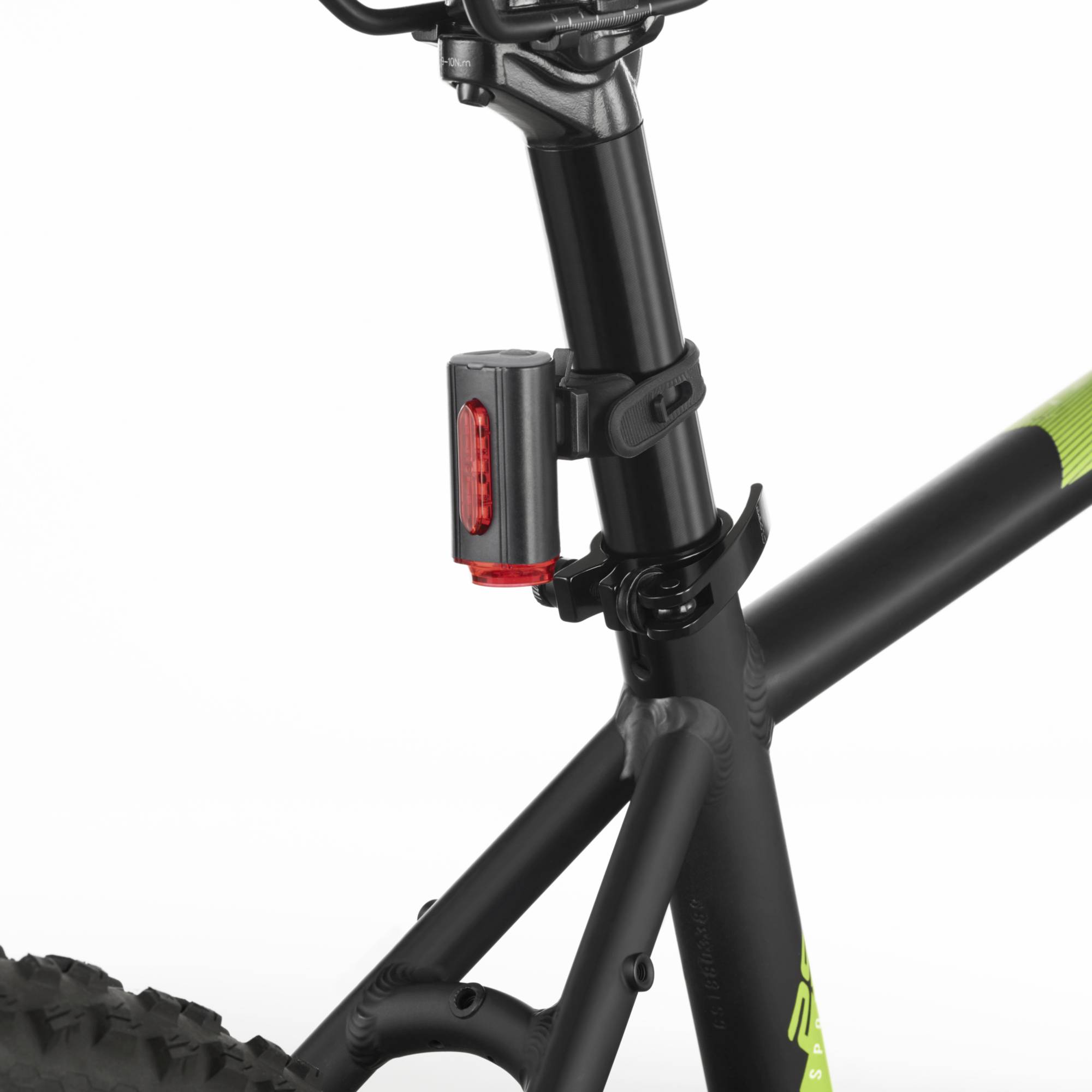 Detailní záběr cyklistického sedla s černou sedlovkou a připevněným červeným zadním světlem. Jsou vidět části rámu a pneumatiky.