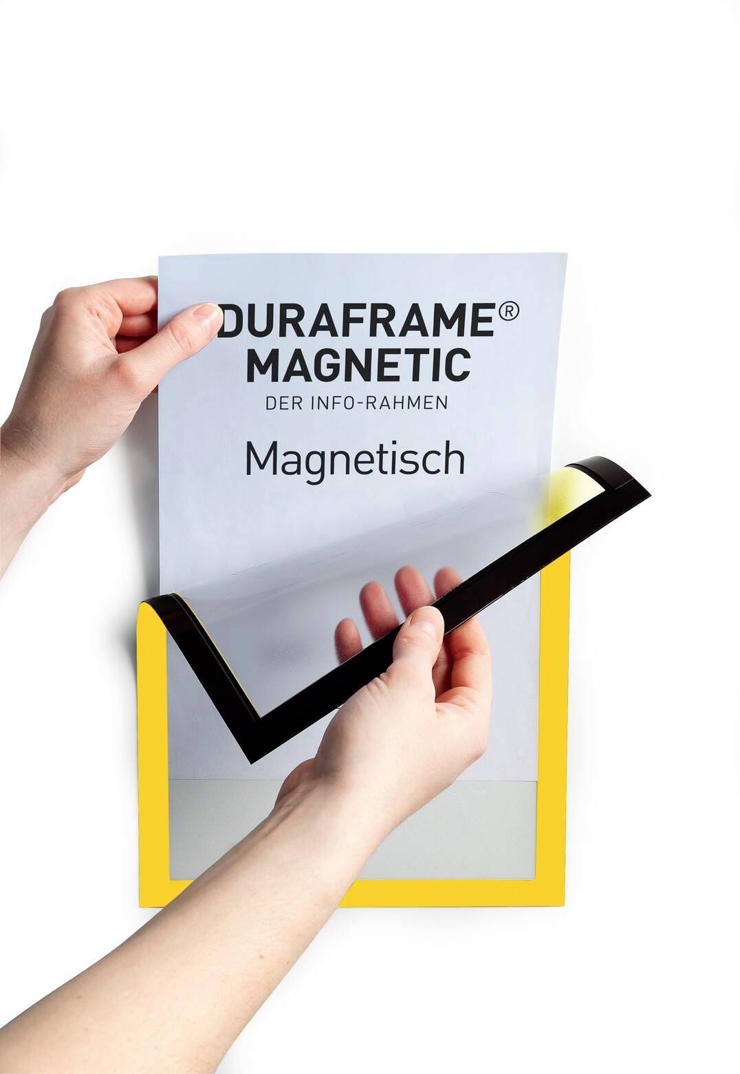 Ruce drží žlutý magnetický rámeček nazvaný 'Duraframe Magnetic', zatímco je vkládána potištěná fólie.