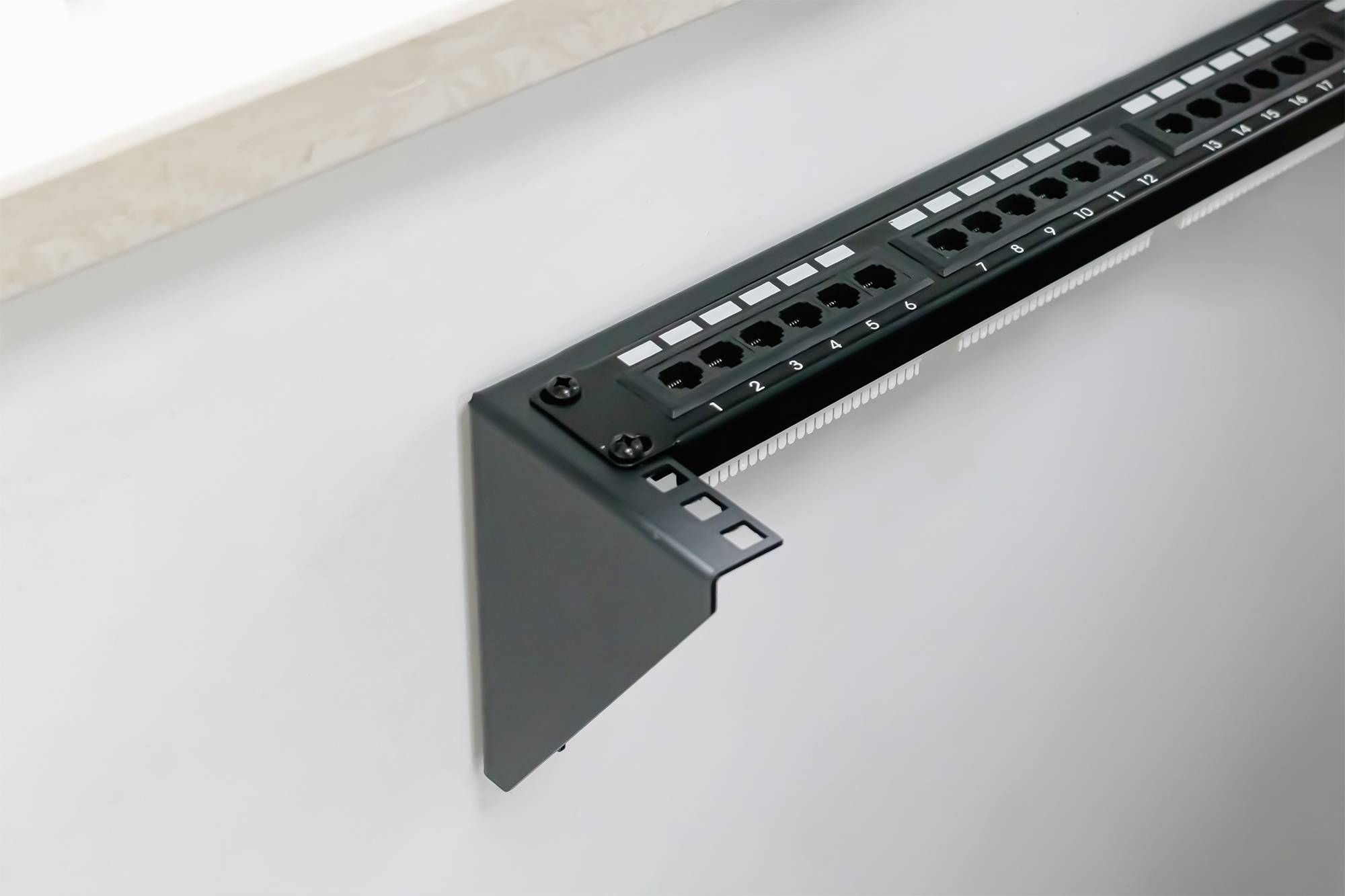 Patch panel namontovaný na stěně, s očíslovanými porty pro organizaci síťových připojení.